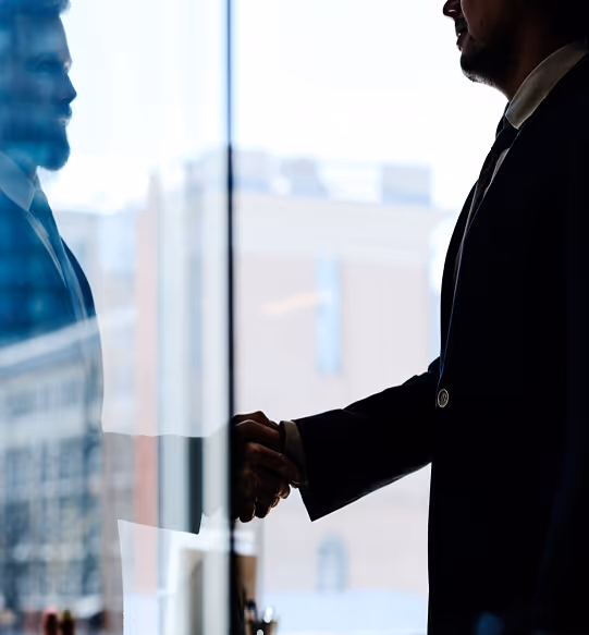 Deux hommes en costume se serrant la main devant une fenêtre avec une vue urbaine floue.