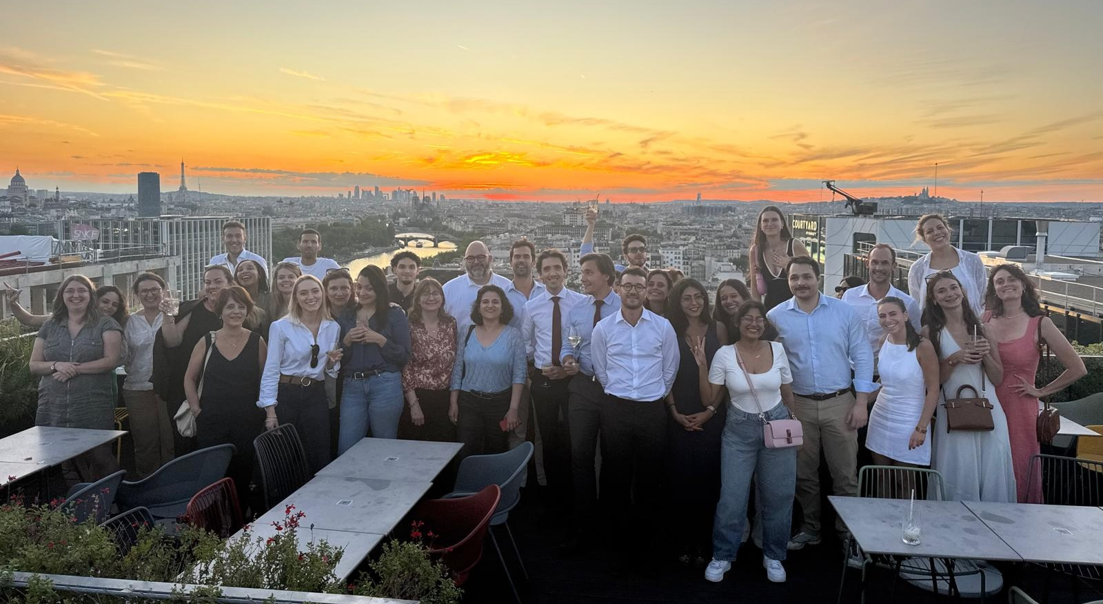 Groupe de personnes posant pour une photo lors d'un coucher de soleil sur une terrasse avec vue sur Paris, incluant la Seine et la Tour Eiffel à l'arrière-plan.