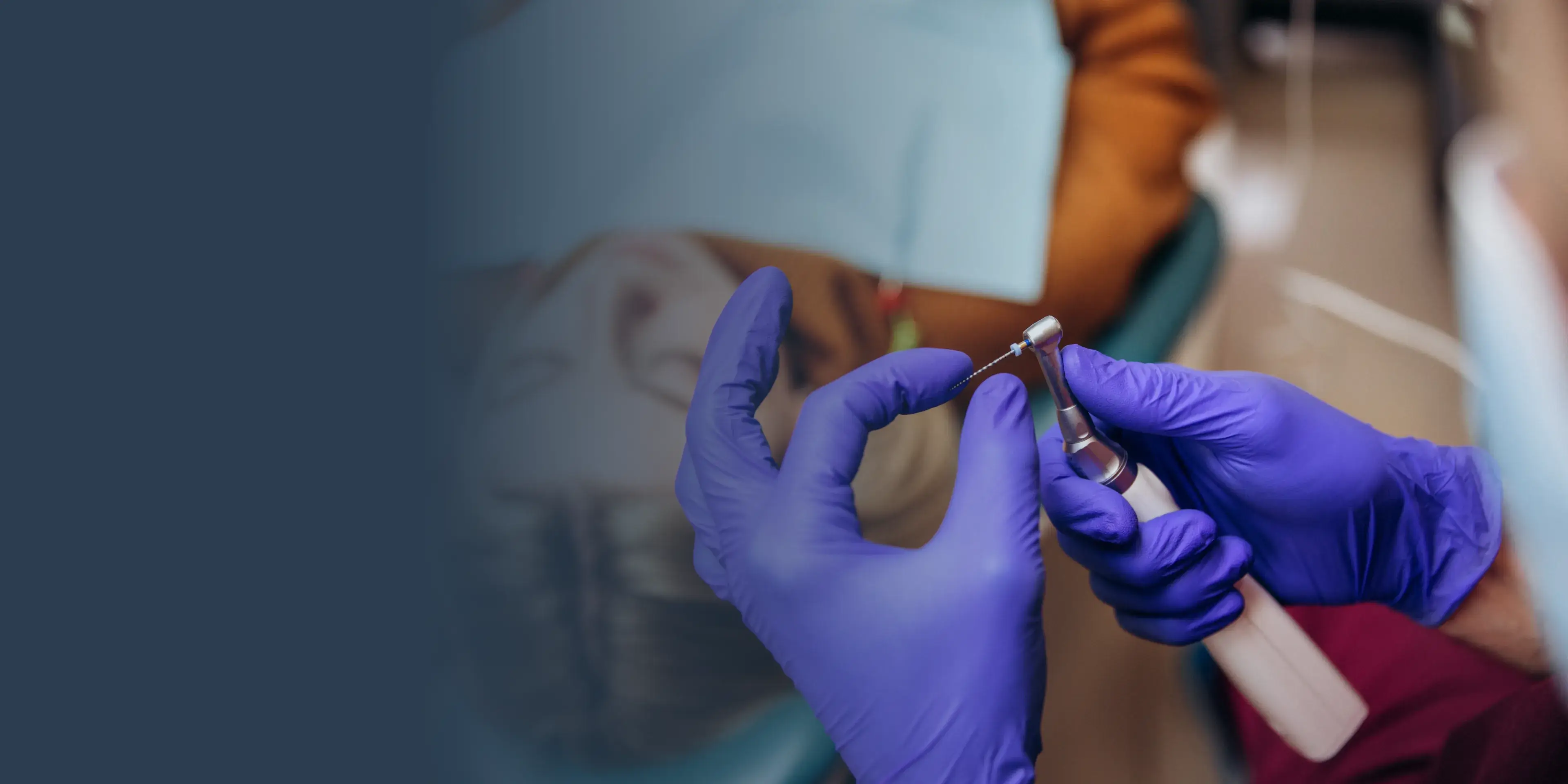 Dentist wearing purple gloves holding a dental drill and a tiny root canal file.