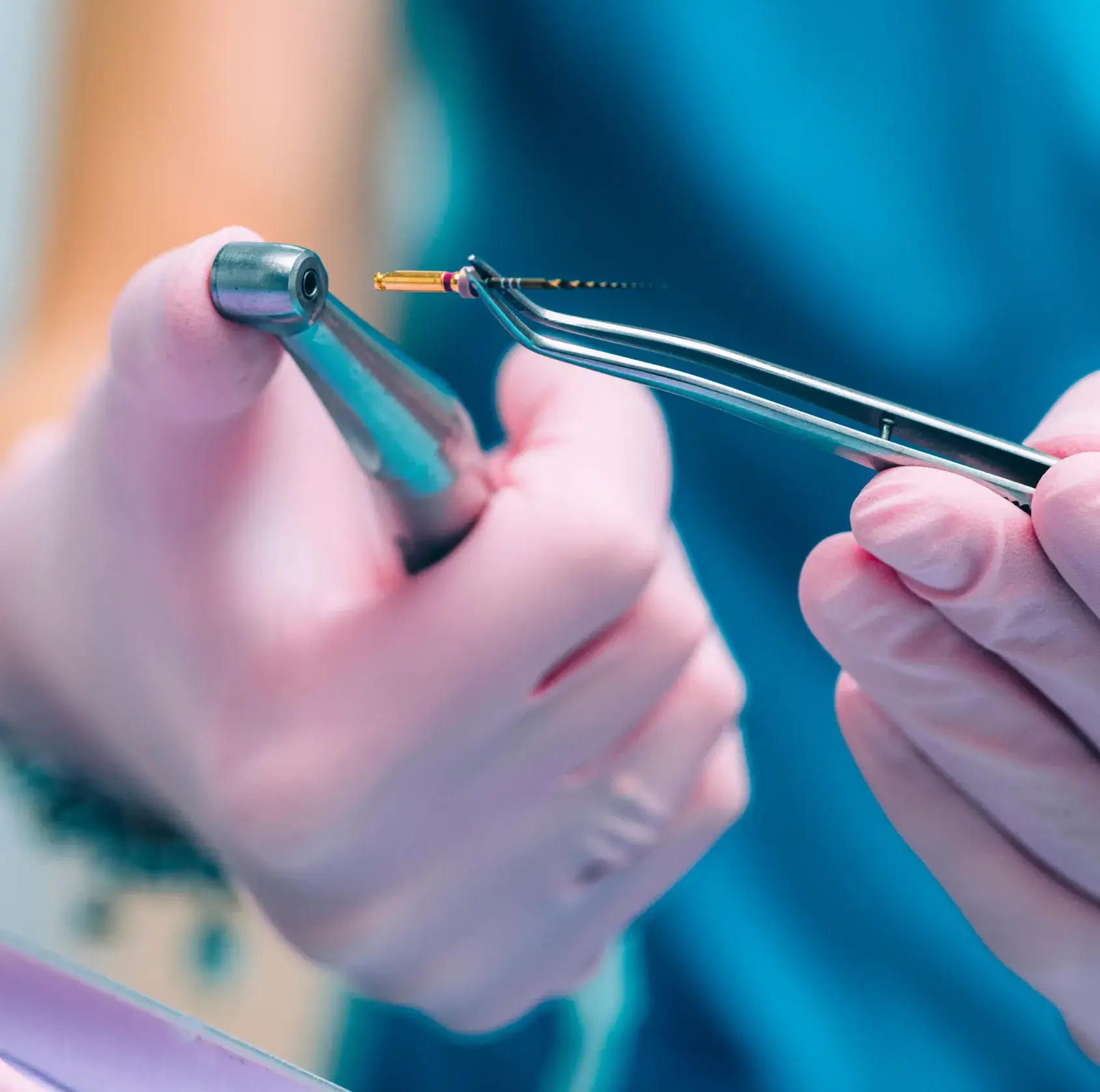 Gloved hands holding dental tool and tweezers with a root canal file tip.