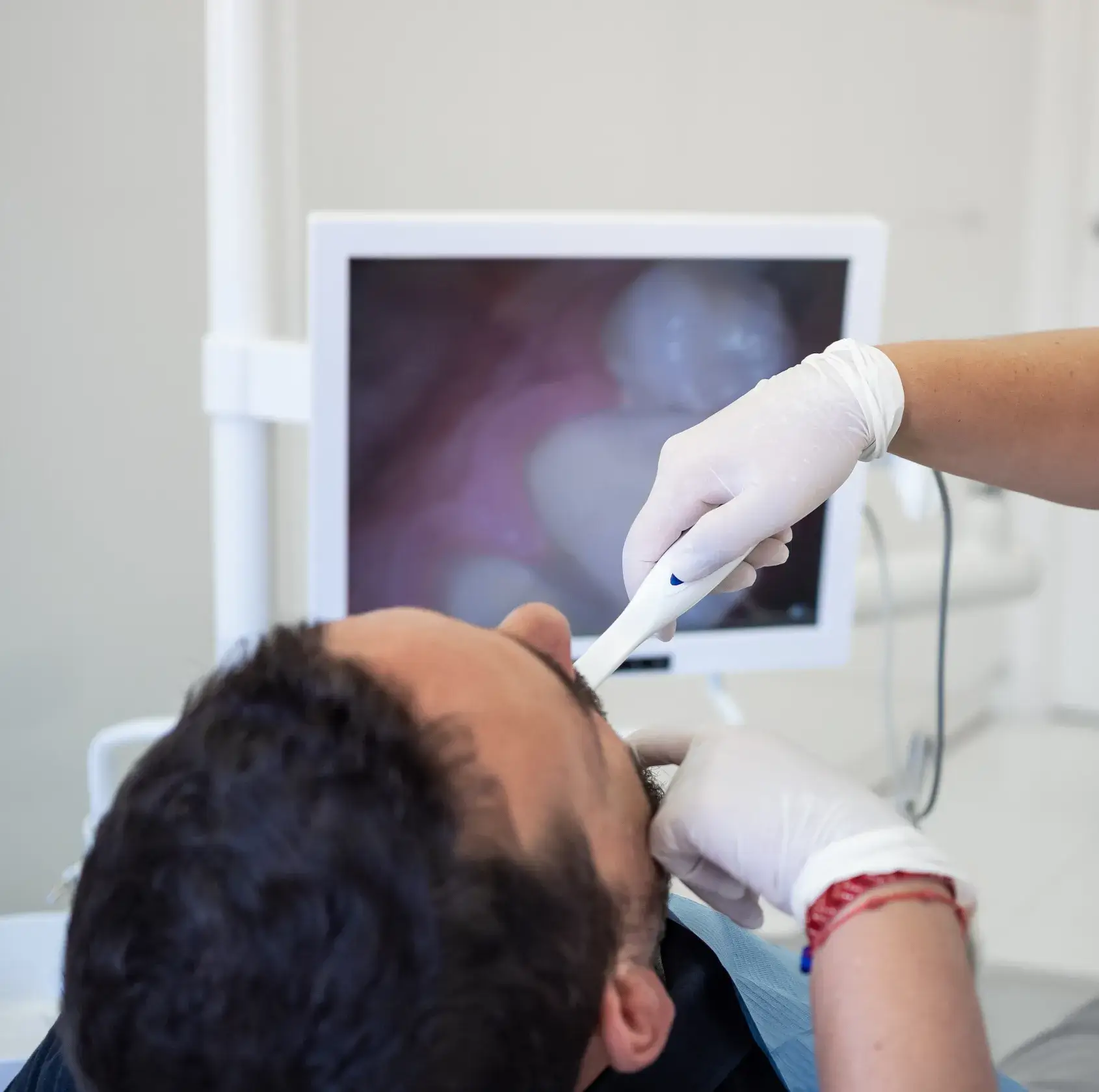 Dentist using intraoral camera to examine a male patient’s teeth shown on a monitor.