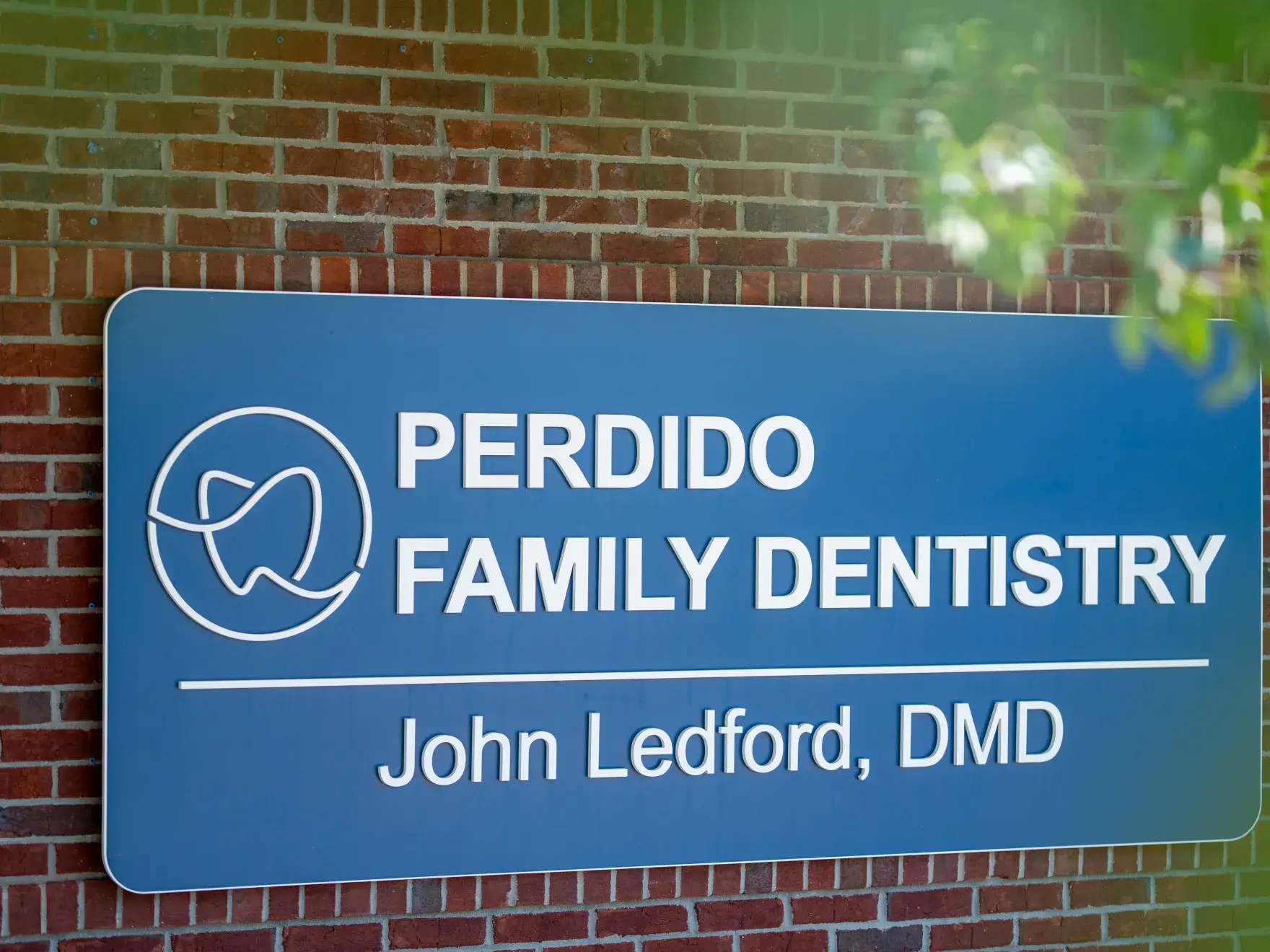 Blue sign on a brick wall reads Perdido Family Dentistry, John Ledford, DMD, with a tooth logo.