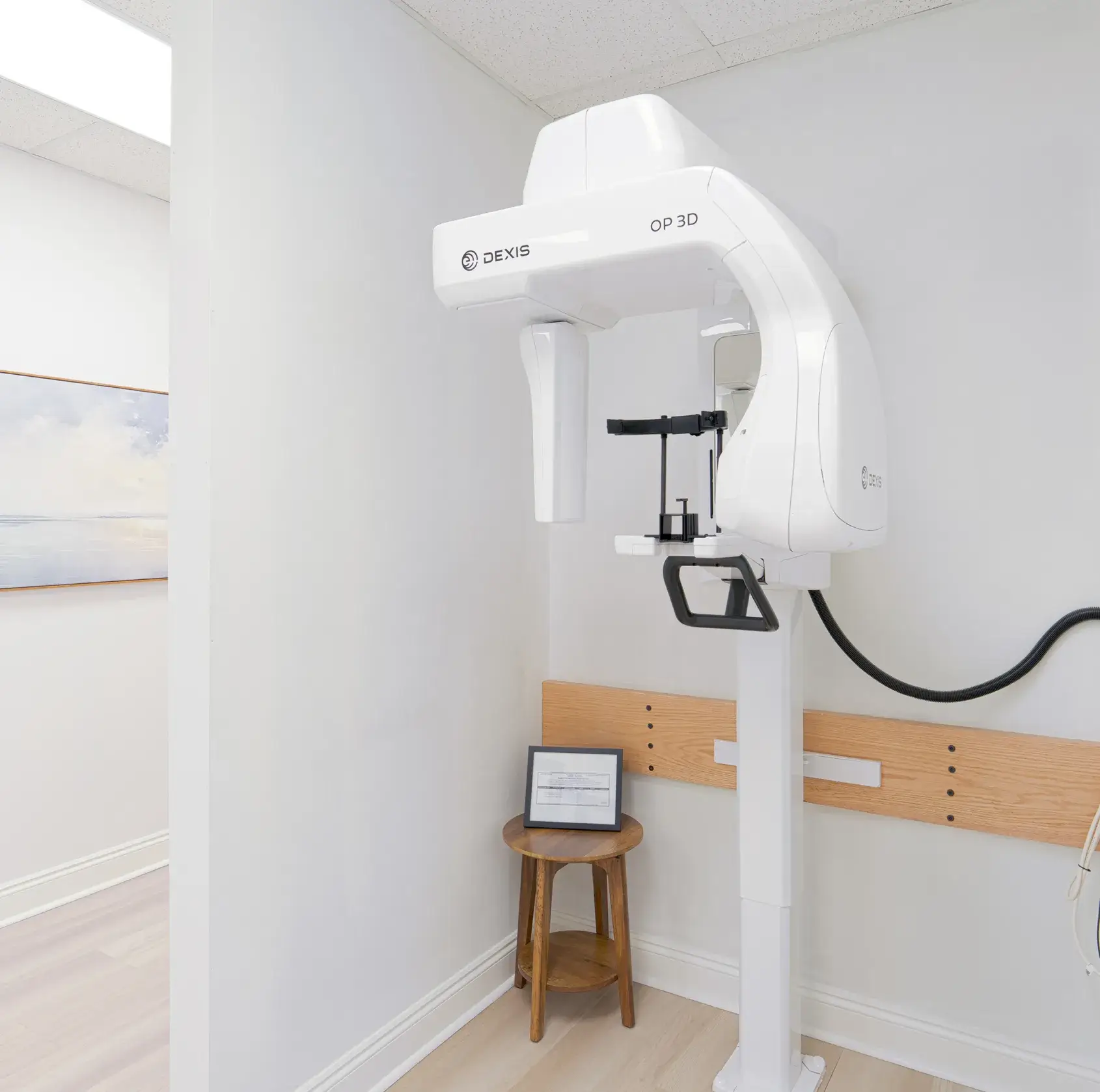 White Dexis OP 3D dental imaging machine in a clean room with light walls and wooden stool.