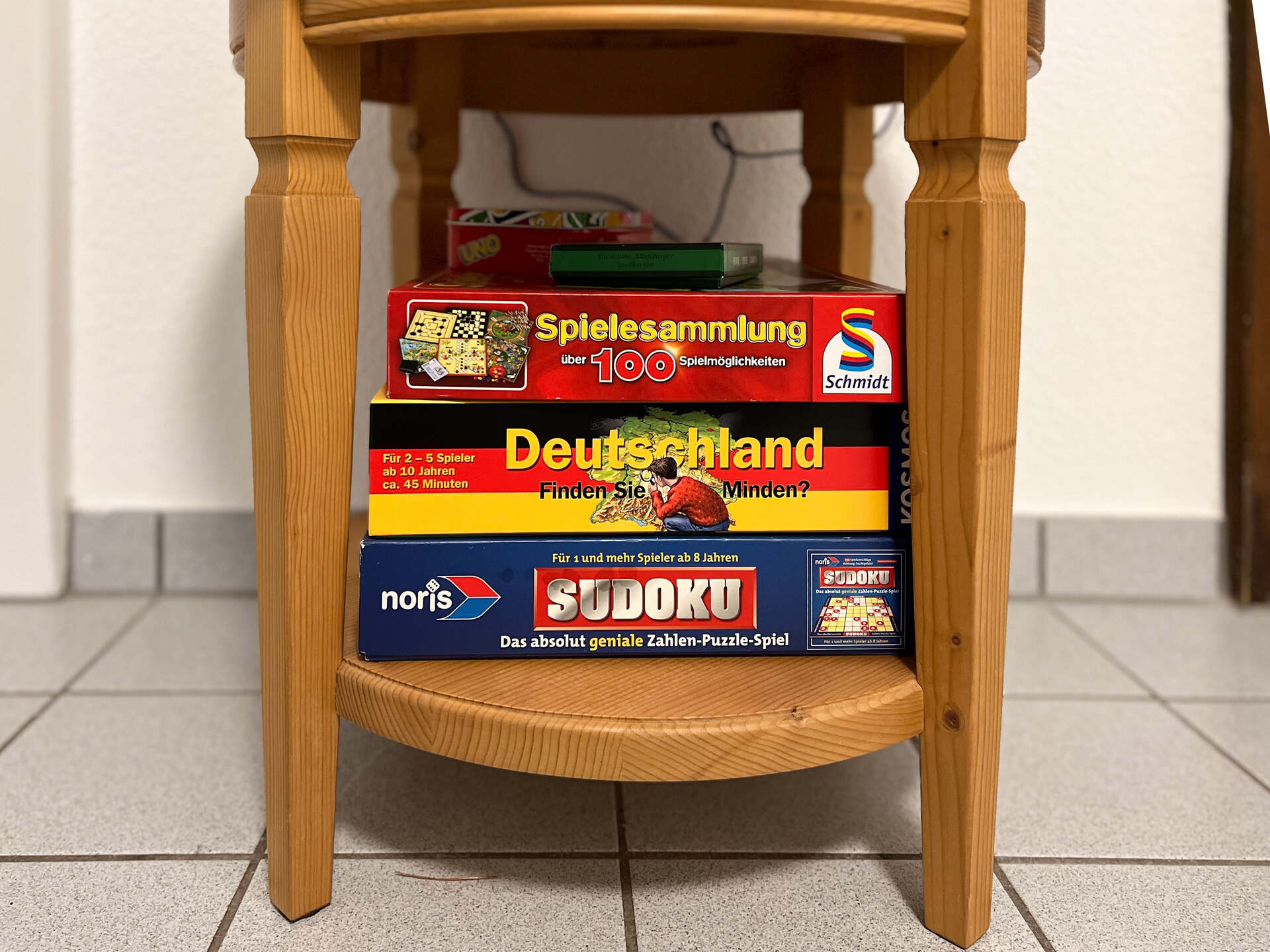 Spielesammlung mit Brettspielen unter einem kleinen Holztisch im Eingangsbereich der Ferienwohnung