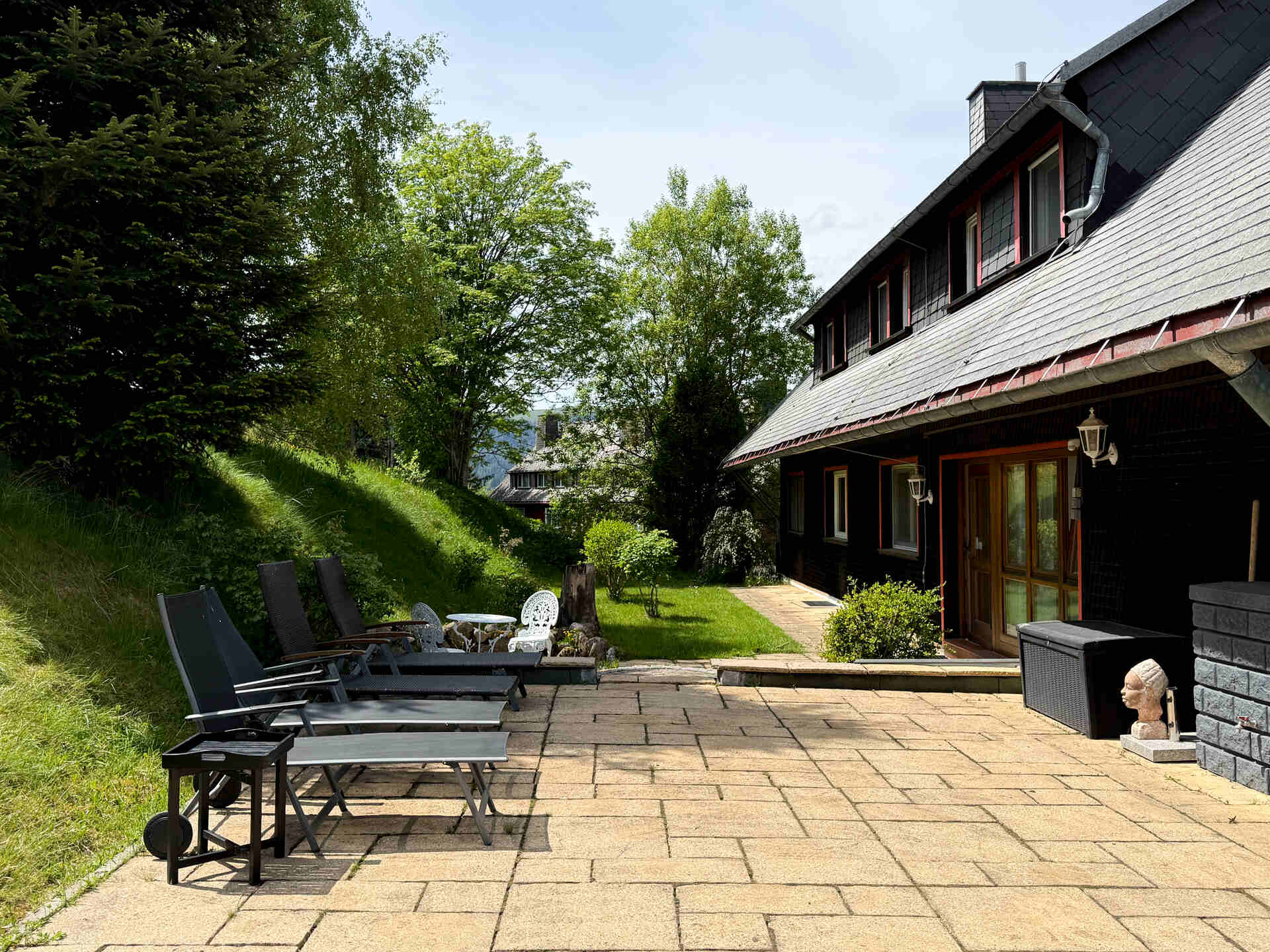 Blick auf die Sonnenterrasse mit mehreren Liegestuehlen und angrenzender Wiese vor dem Haus