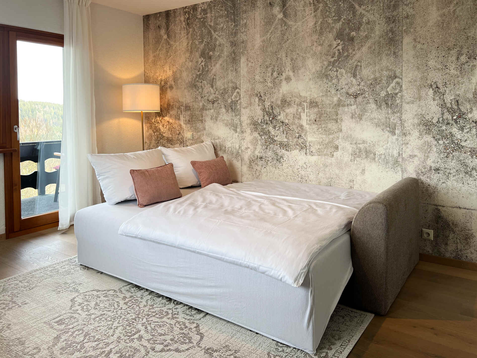 Schlafsofa in Boxspring Qualität mit Kissen vor strukturierter WandGraues Sofa vor strukturierter Wand mit Deko-Kissen