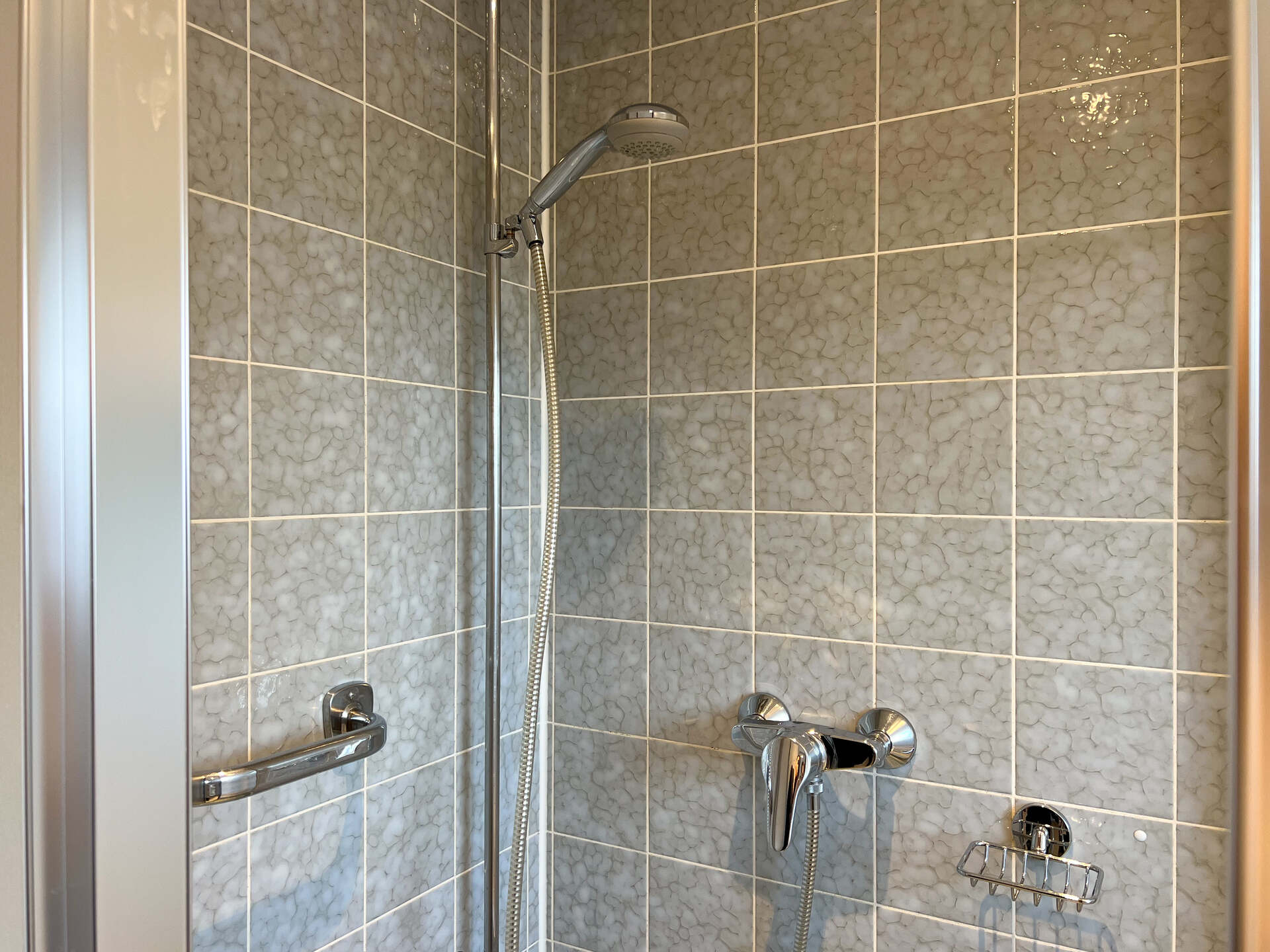 Dusche mit Handbrause und grauen Fliesen