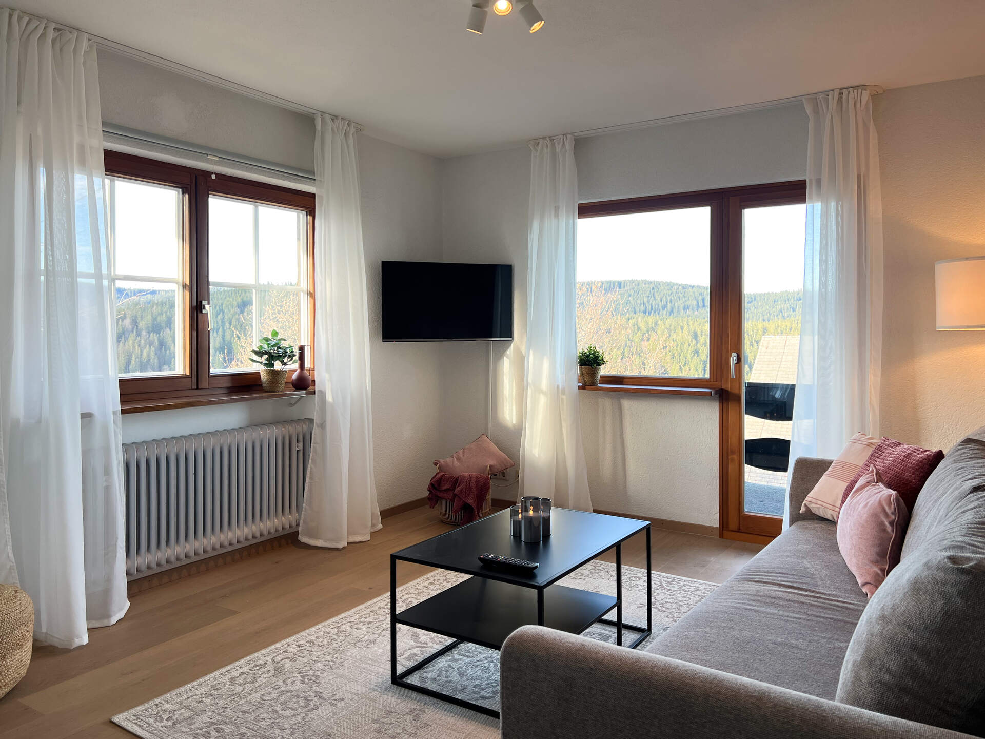 Helles Wohnzimmer mit Sofa, TV und Panoramafenstern