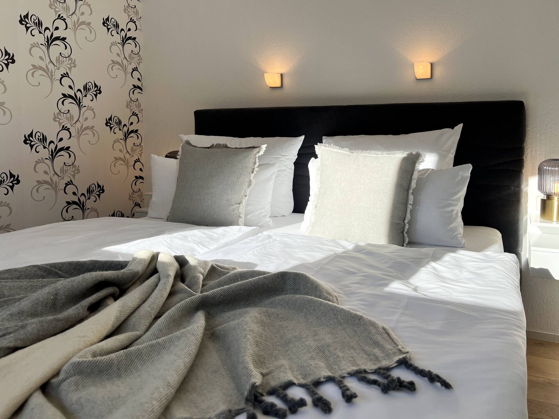 Doppelbett mit Zierkissen und Tapetenwand