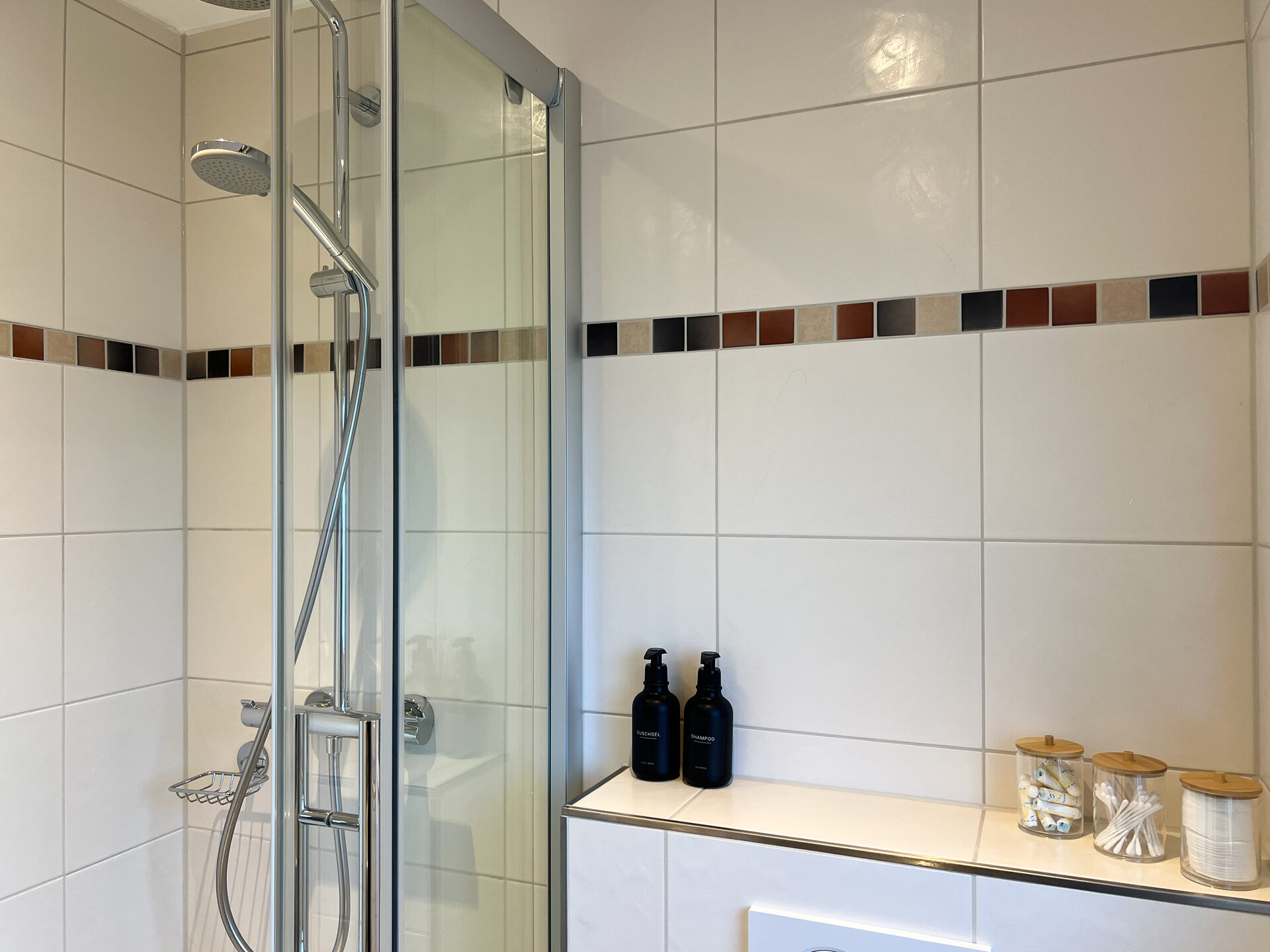 Dusche mit Glaswand und buntem Fliesenband