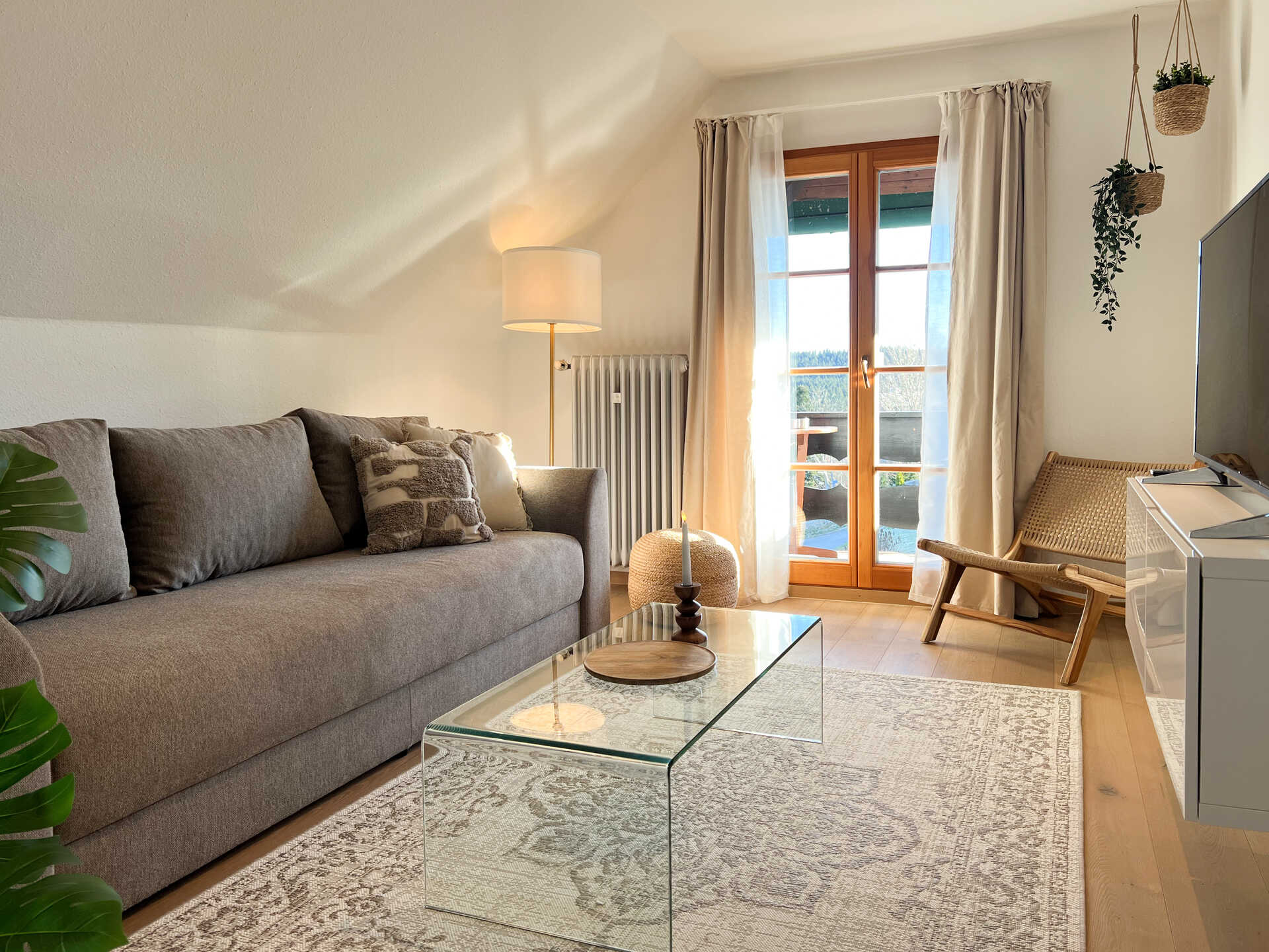 Wohnzimmer mit Sofa, Glastisch und Balkonblick