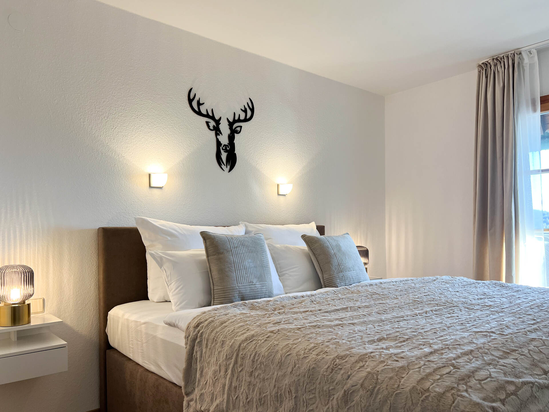 Schlafzimmer mit Boxpring Bett, Fenster und Wanddeko aus Holz