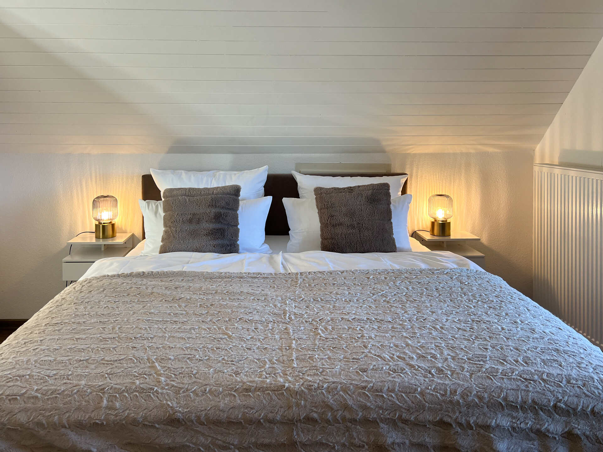 Doppelbett unter Dachschraege mit Nachttischlampen