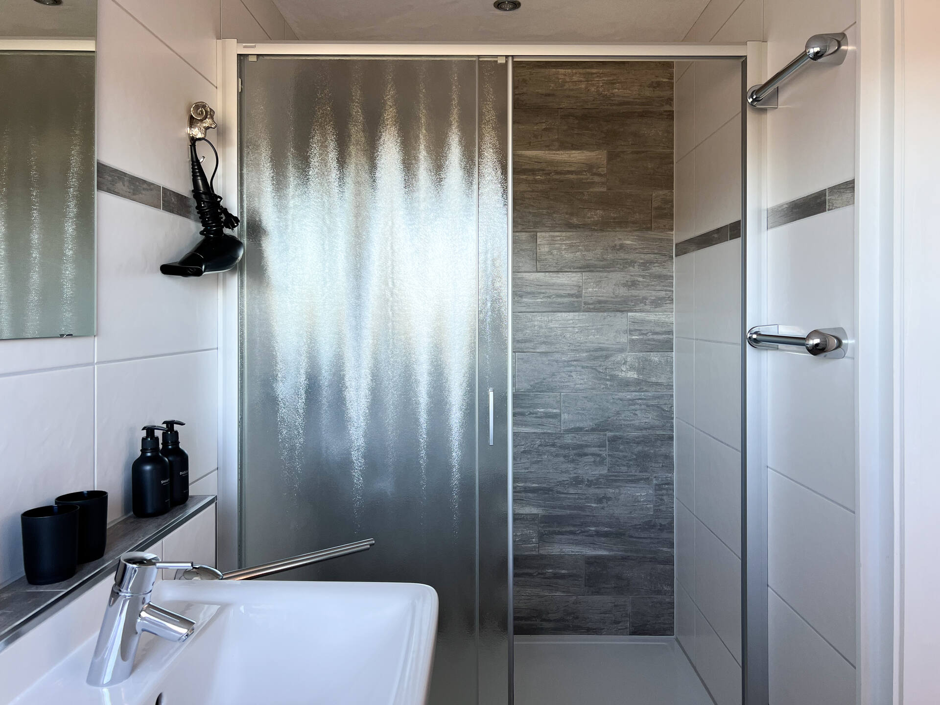 Dusche mit Glaswand und dunklen Fliesen