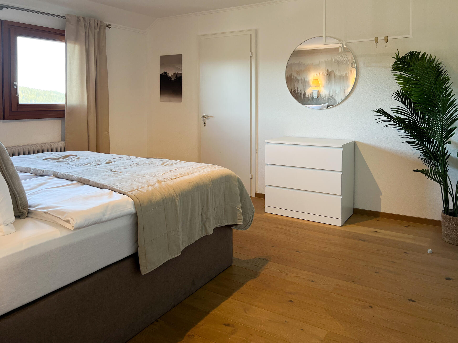 Schlafzimmer mit Kommode, Spiegel und grossem Fenster