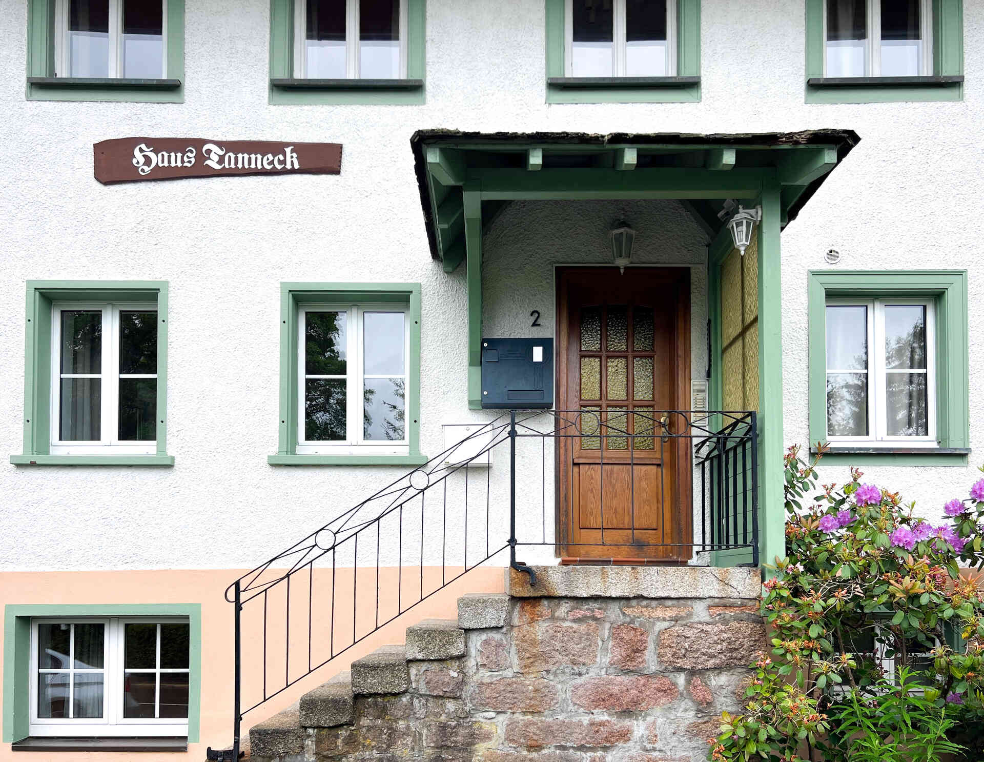 Eingangsbereich des Hauses mit gruenen Fensterrahmen, Treppe und Holztuer
