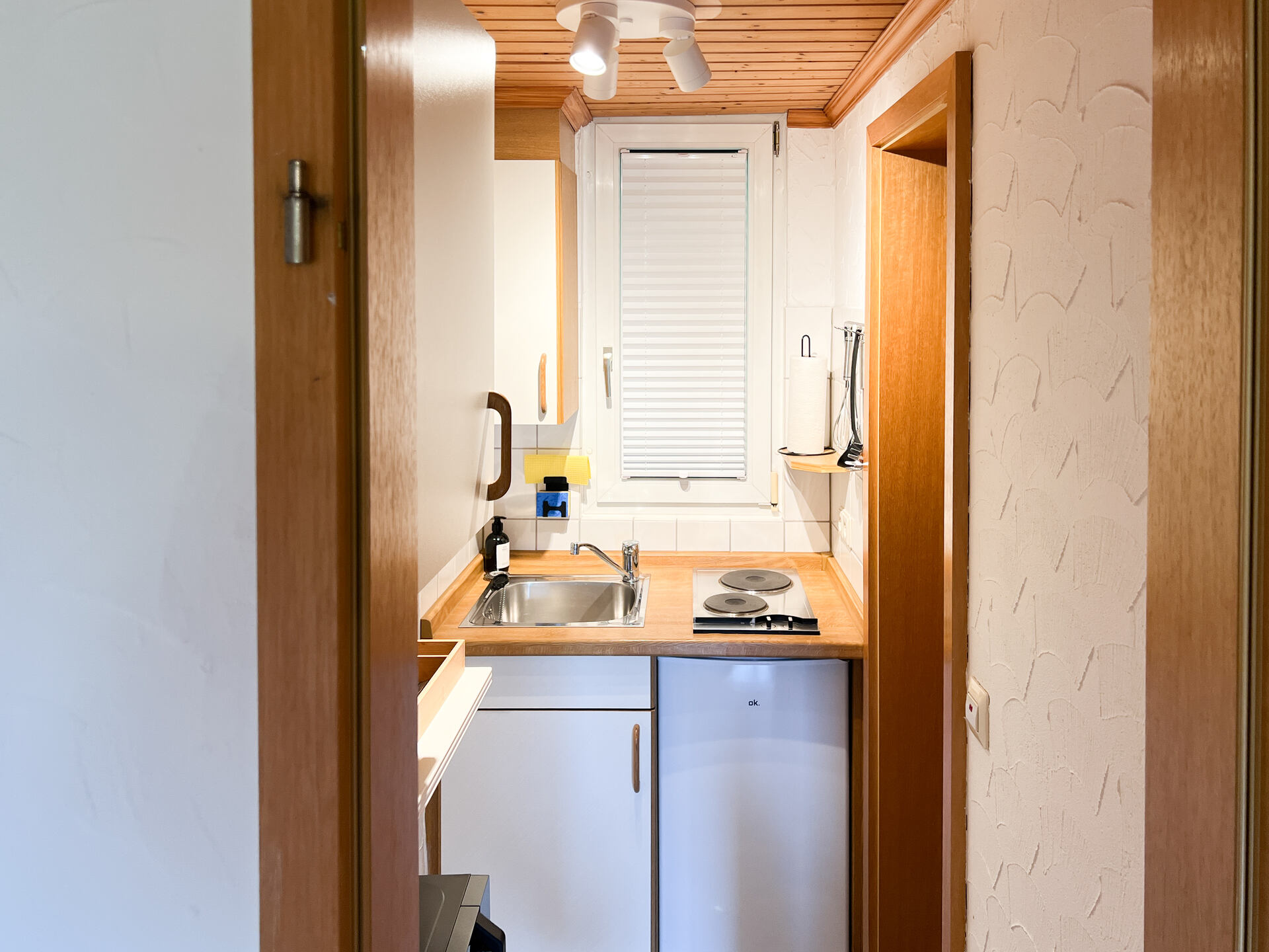 Kompakte Kuechenzeile mit Spuele, Kuehlschrank, Kochfeld und Fenster mit Jalousie