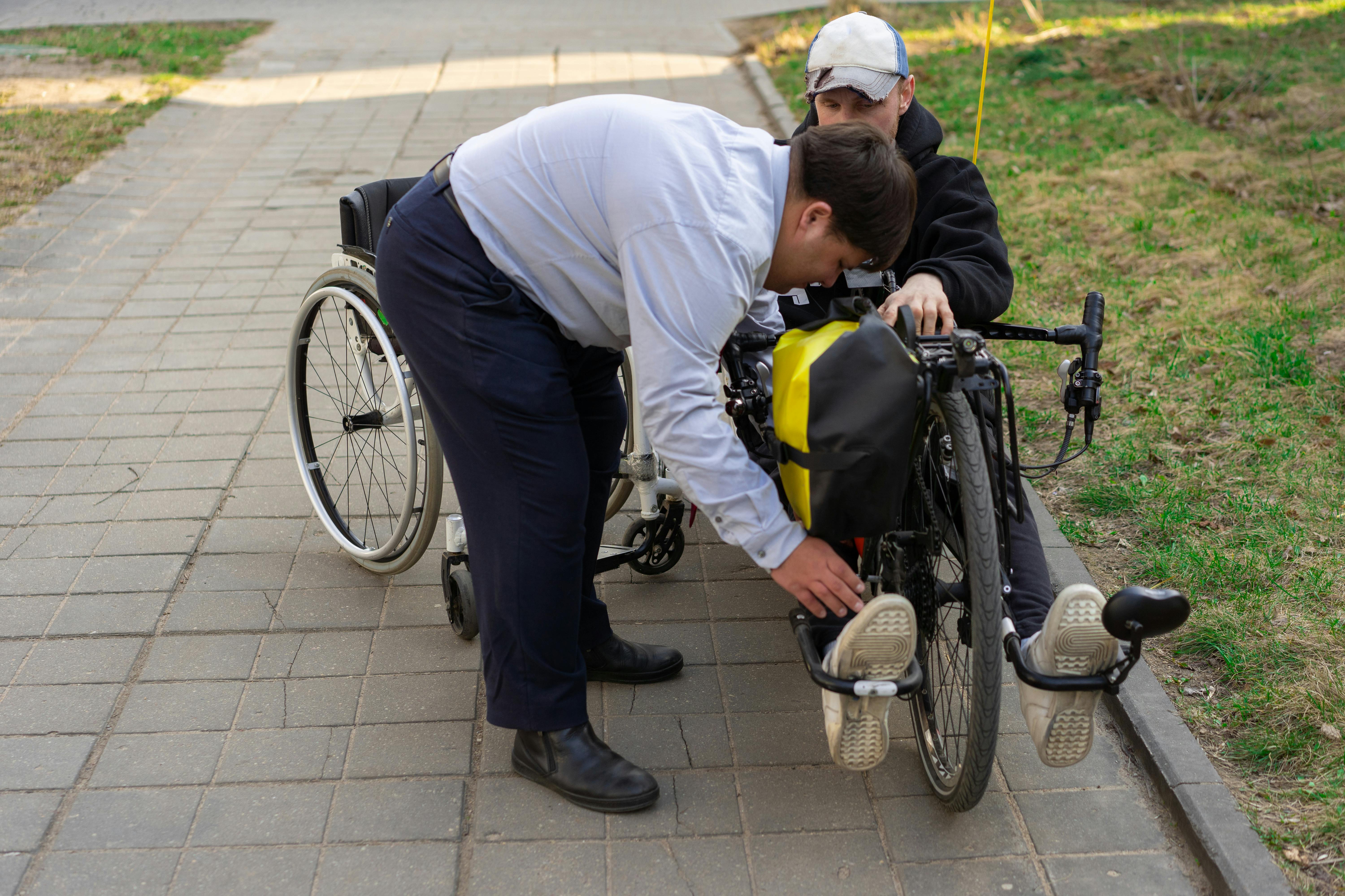 Image of a male Support Worker helping another male into a custom bicycle