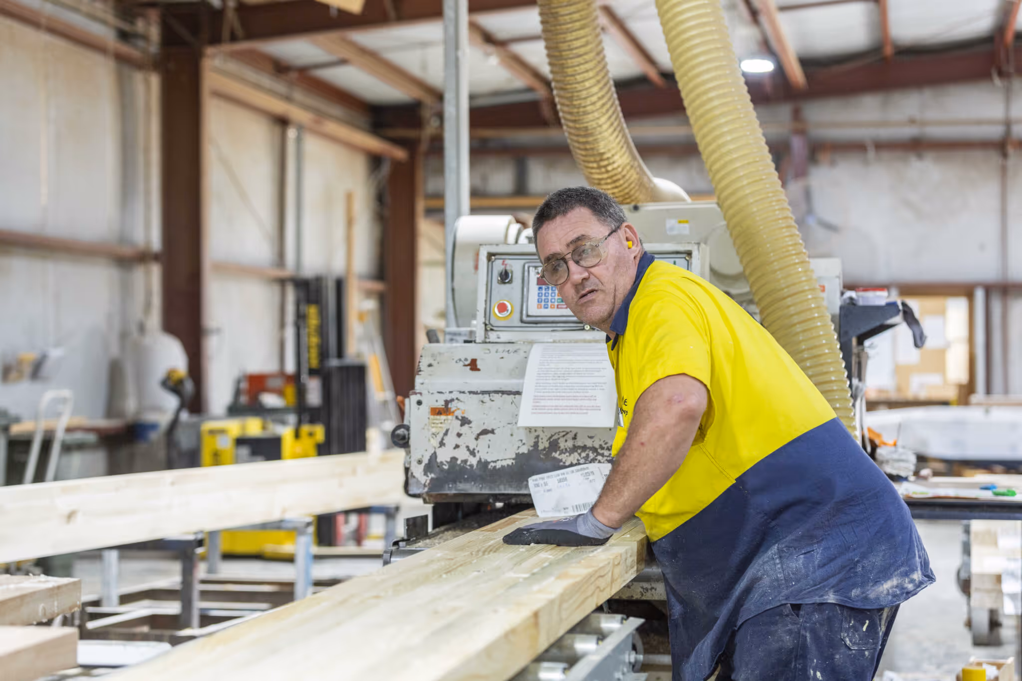 A man in a fluro shirt watching a timber beam go through machinery