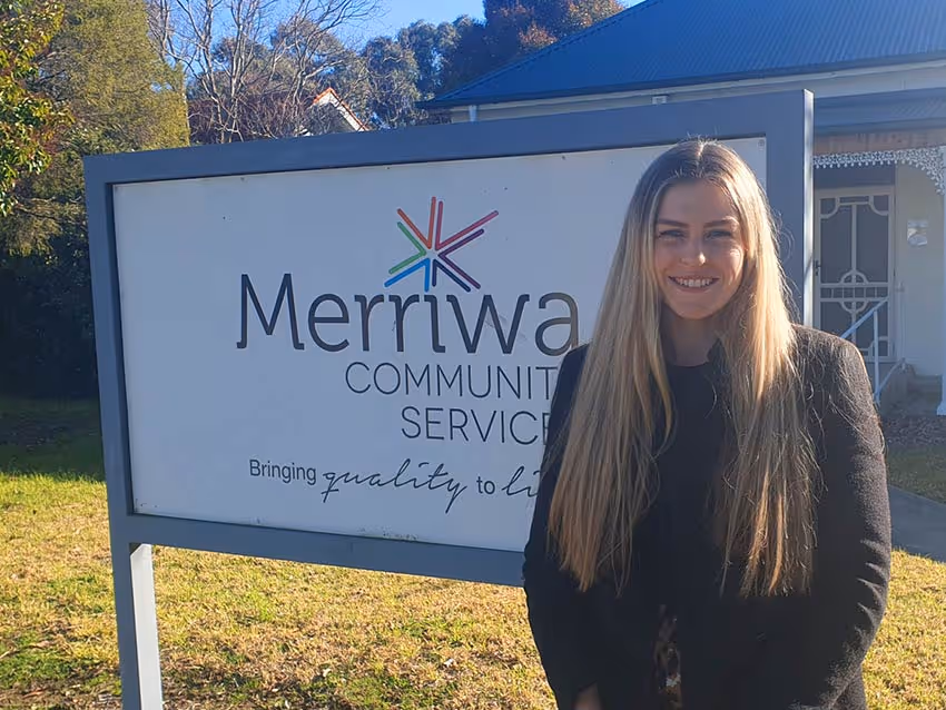 A young lady standing in front of a Merriwa Community Services sign