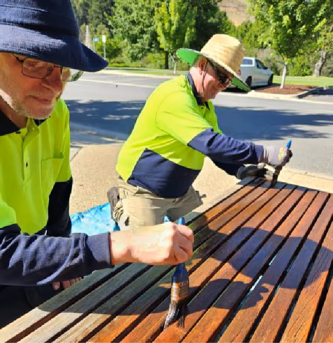 two people brushing oil onto a timber bench