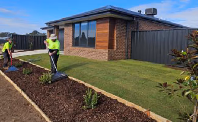 A house with a garden in front of it, with two people doing landscaping