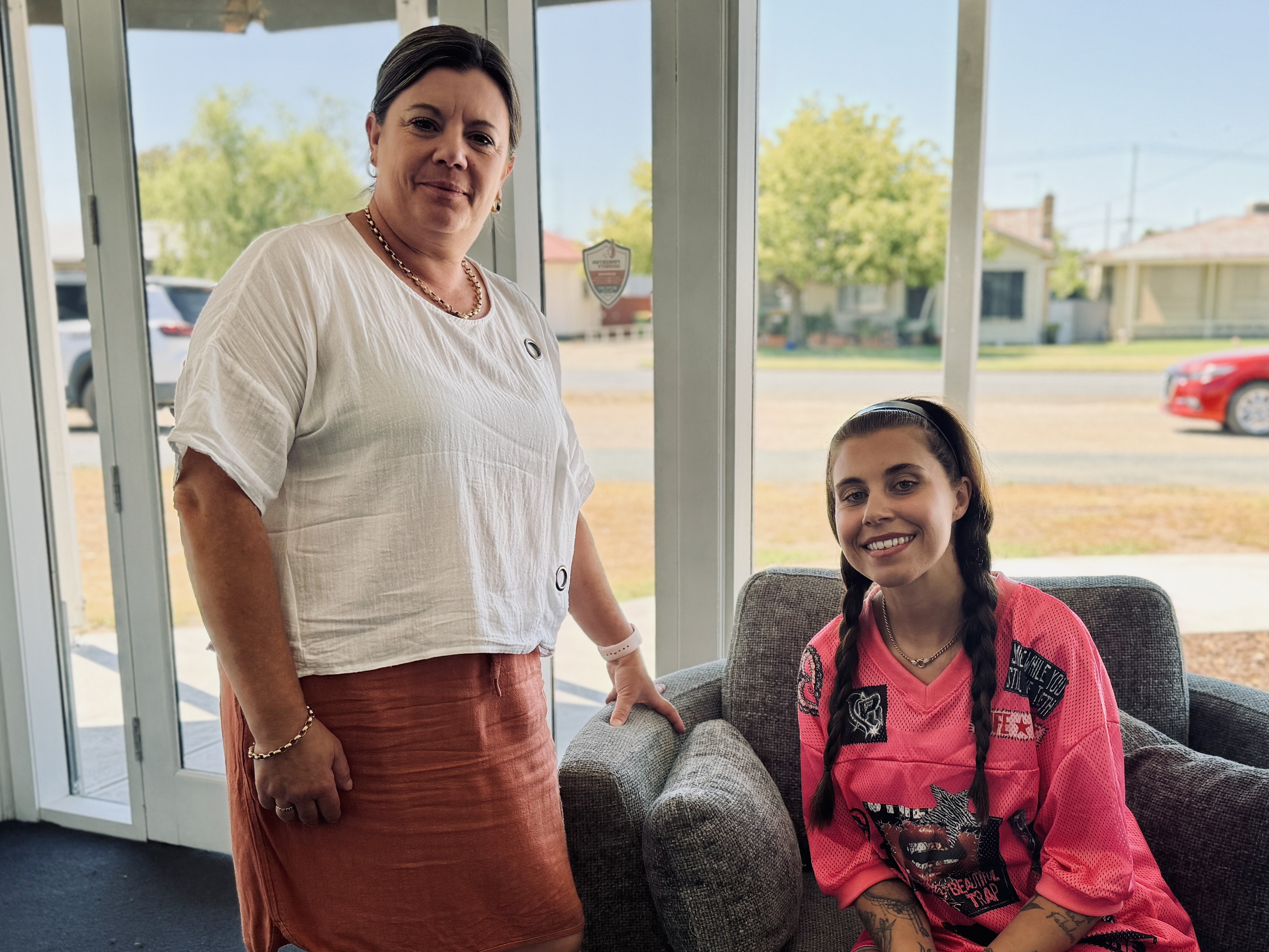 One person sitting down and one standing next to the chair.
