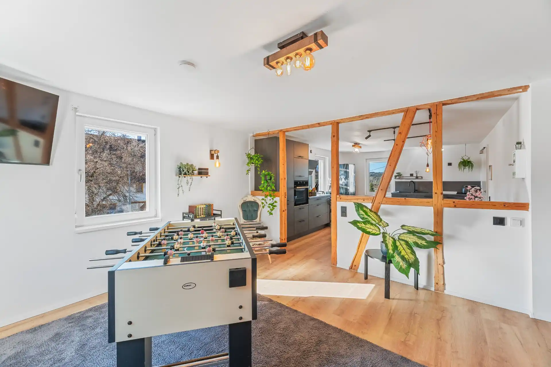 Wohnzimmer mit Tischkicker und hinter dem Fachwerk zwei Esstische im Hintergrund die Küche