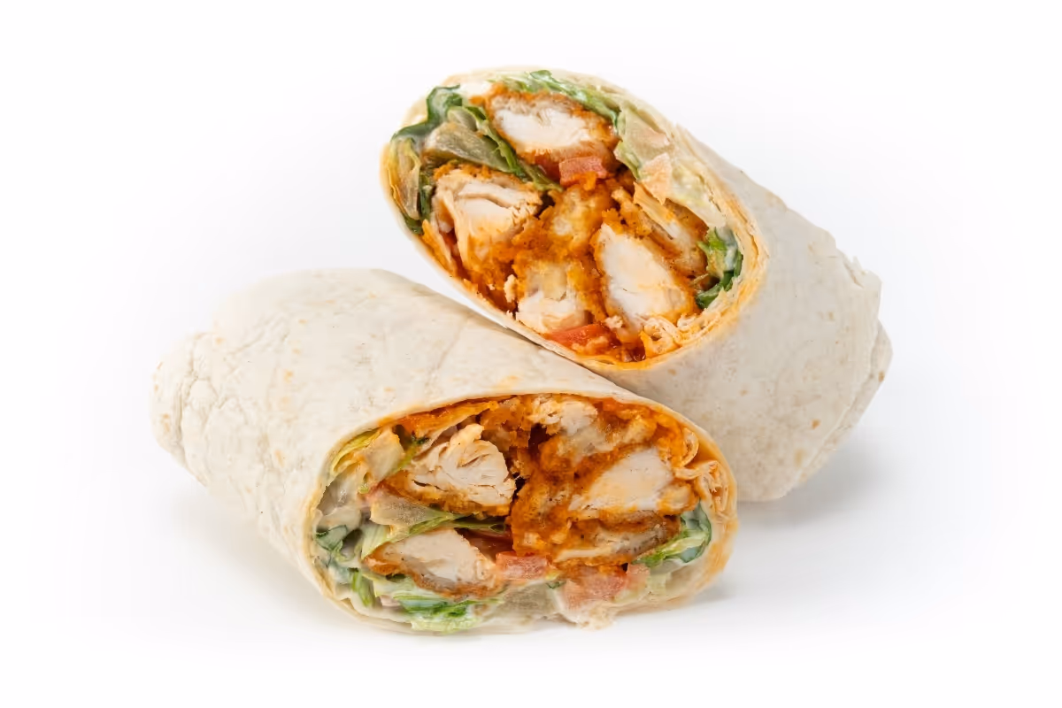 A chicken wrap cut in half, showing lettuce, tomato, and crispy chicken pieces inside a flour tortilla.