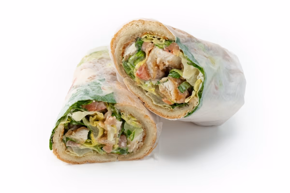 Two halves of a sandwich with lettuce, tomato, and chicken wrapped in paper on a white background.
