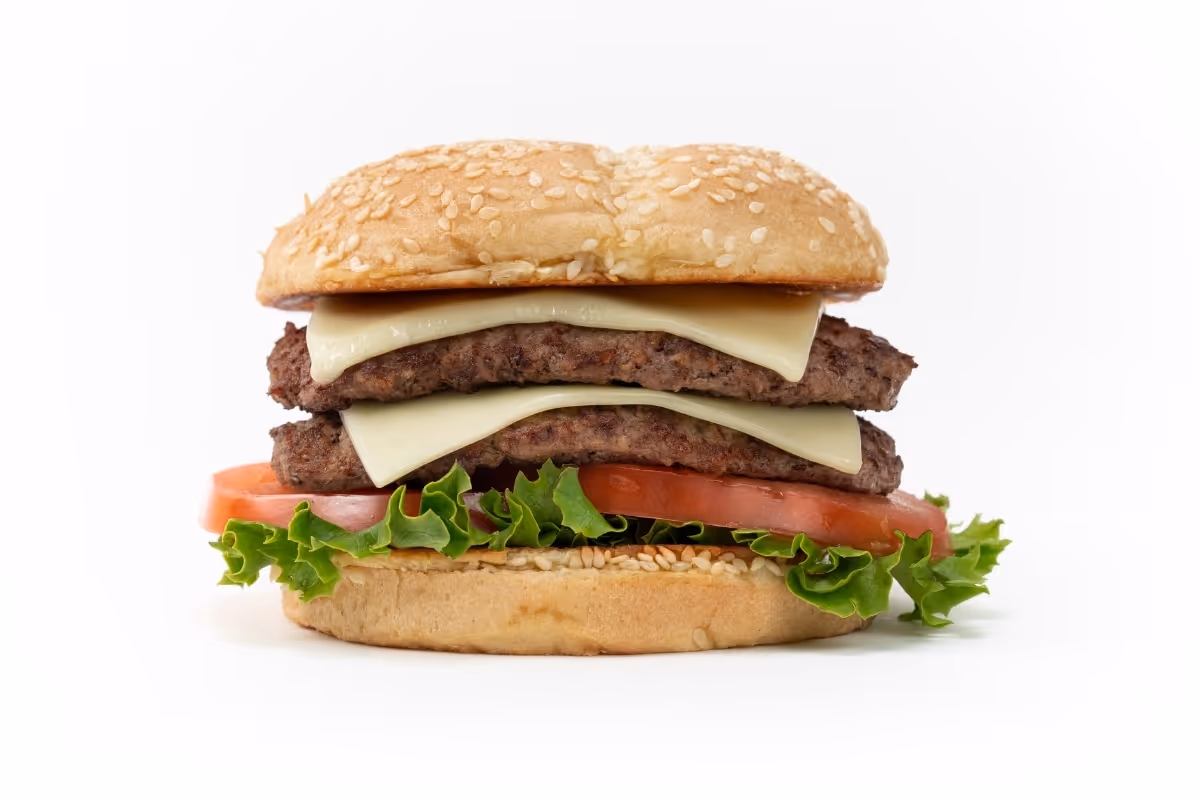 A double cheeseburger with lettuce, tomato, two beef patties, cheese slices, and a sesame seed bun on a white background.