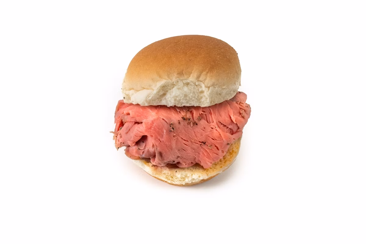 A roast beef sandwich with sliced beef on a plain hamburger bun, isolated on a white background.