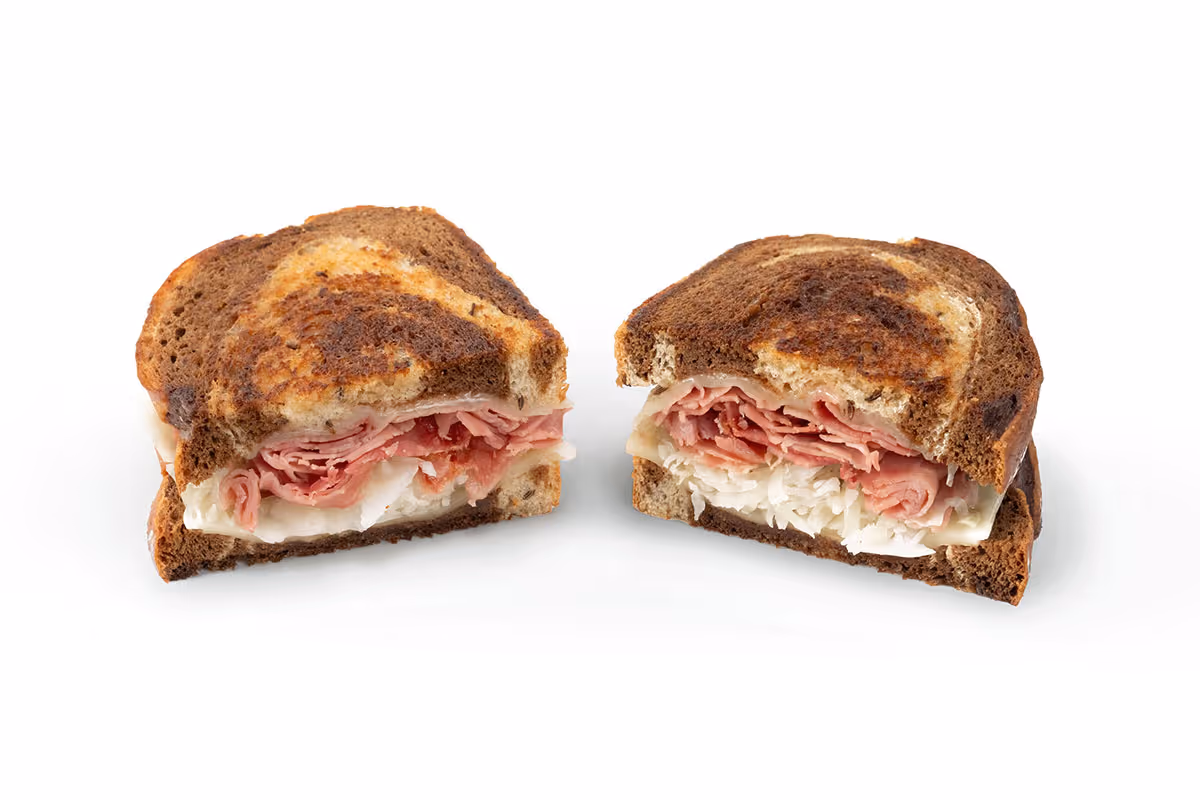 A Reuben sandwich cut in half, showing layers of corned beef, sauerkraut, Swiss cheese, and rye bread on a white background.