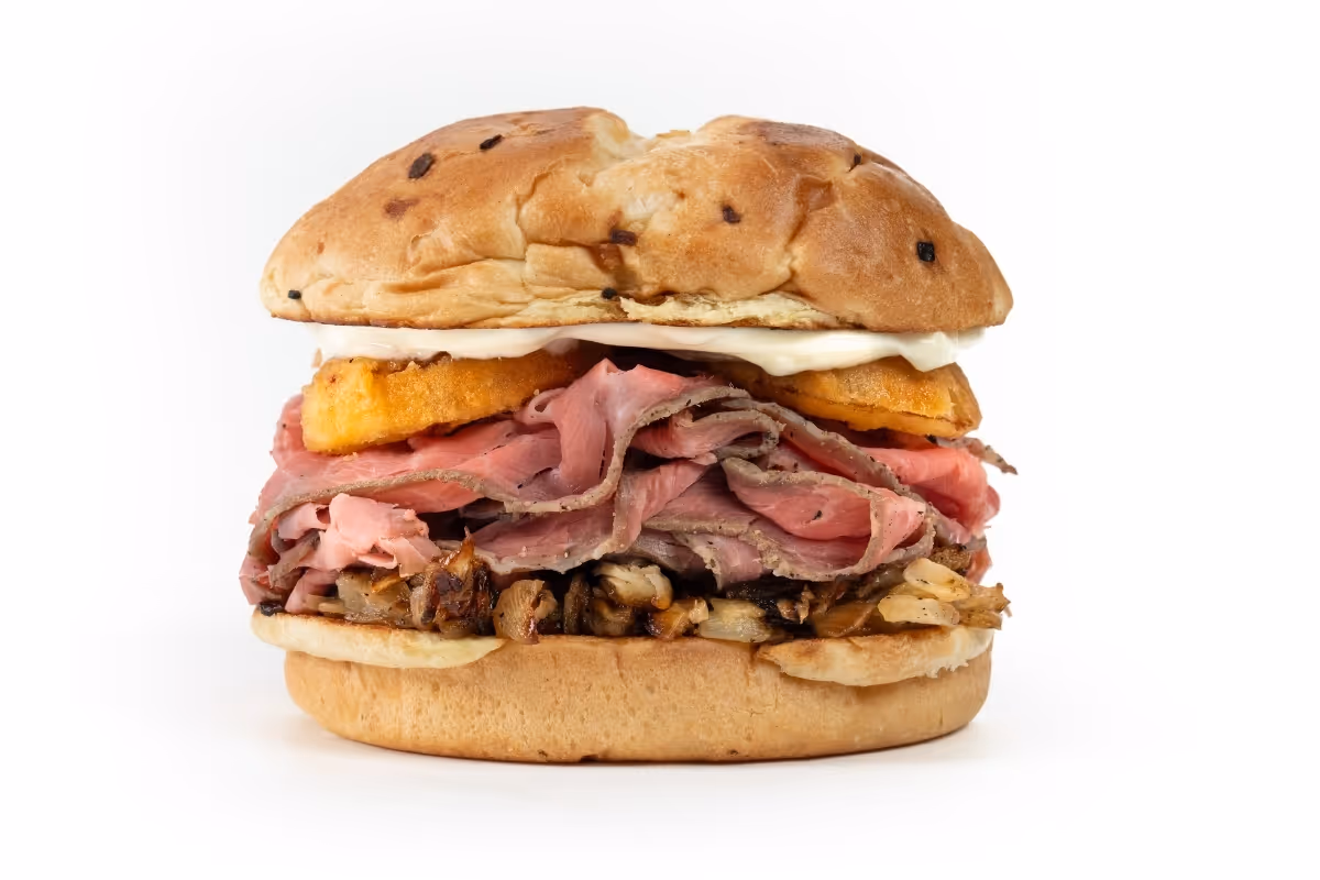 A sandwich with sliced roast beef, fried cheese, onions, and mayo on an onion bun, against a white background.