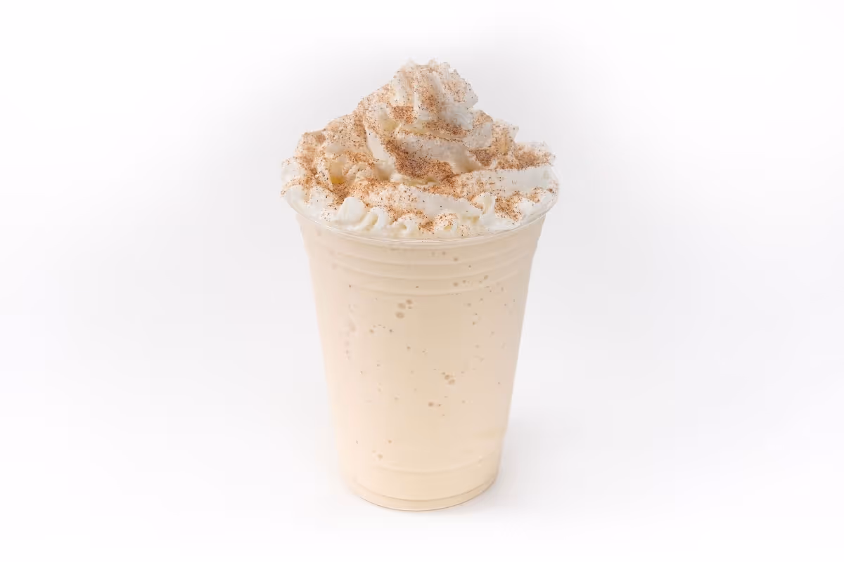 A pumpkin spice frappe in a clear plastic cup topped with whipped cream and sprinkled with cinnamon.