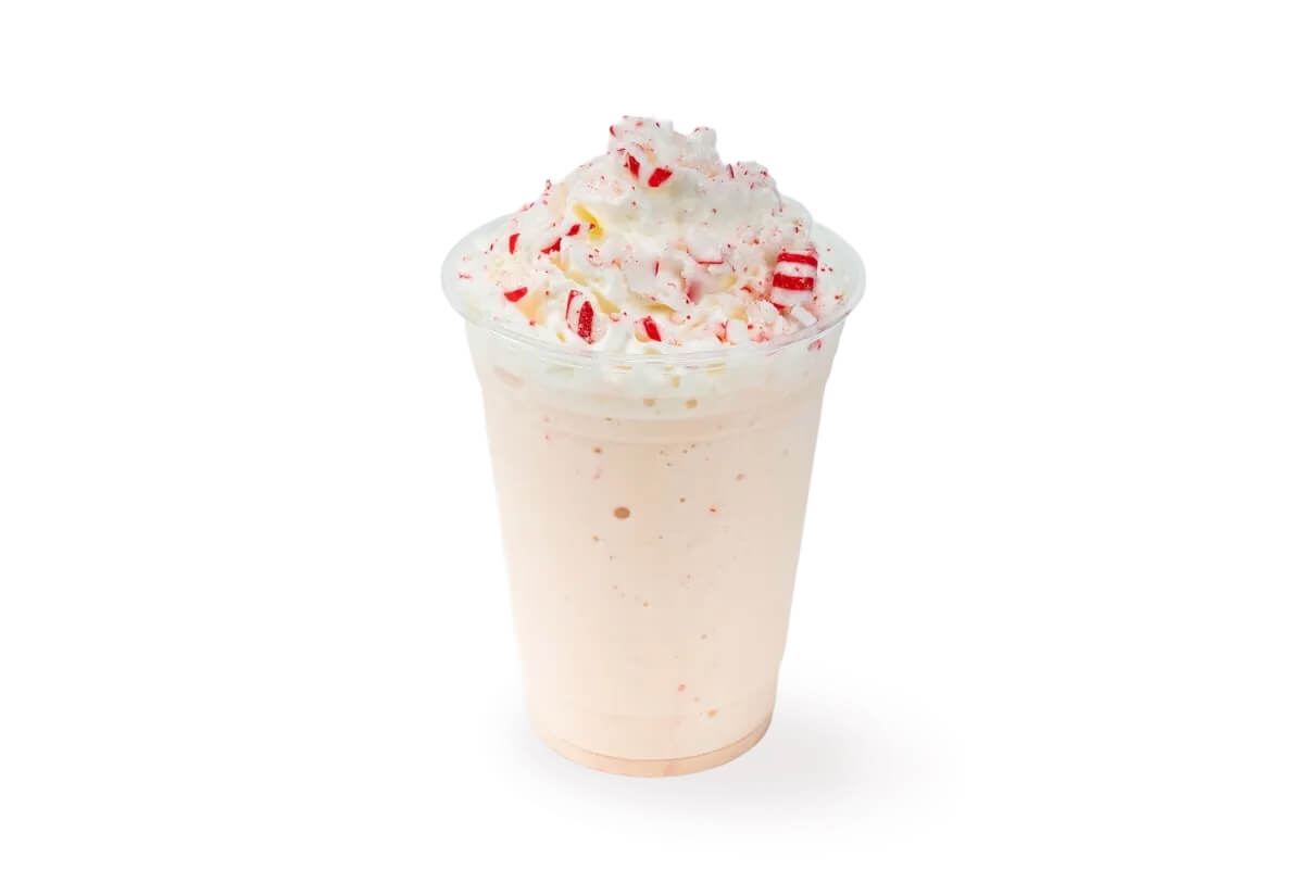 A peppermint milkshake topped with whipped cream and crushed peppermint candies in a clear plastic cup.