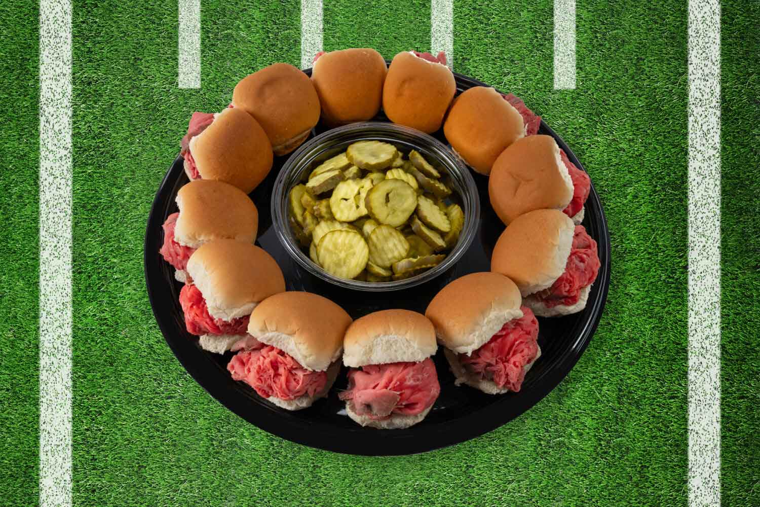 Platter of roast beef sliders with a center bowl of pickles on a football field background.