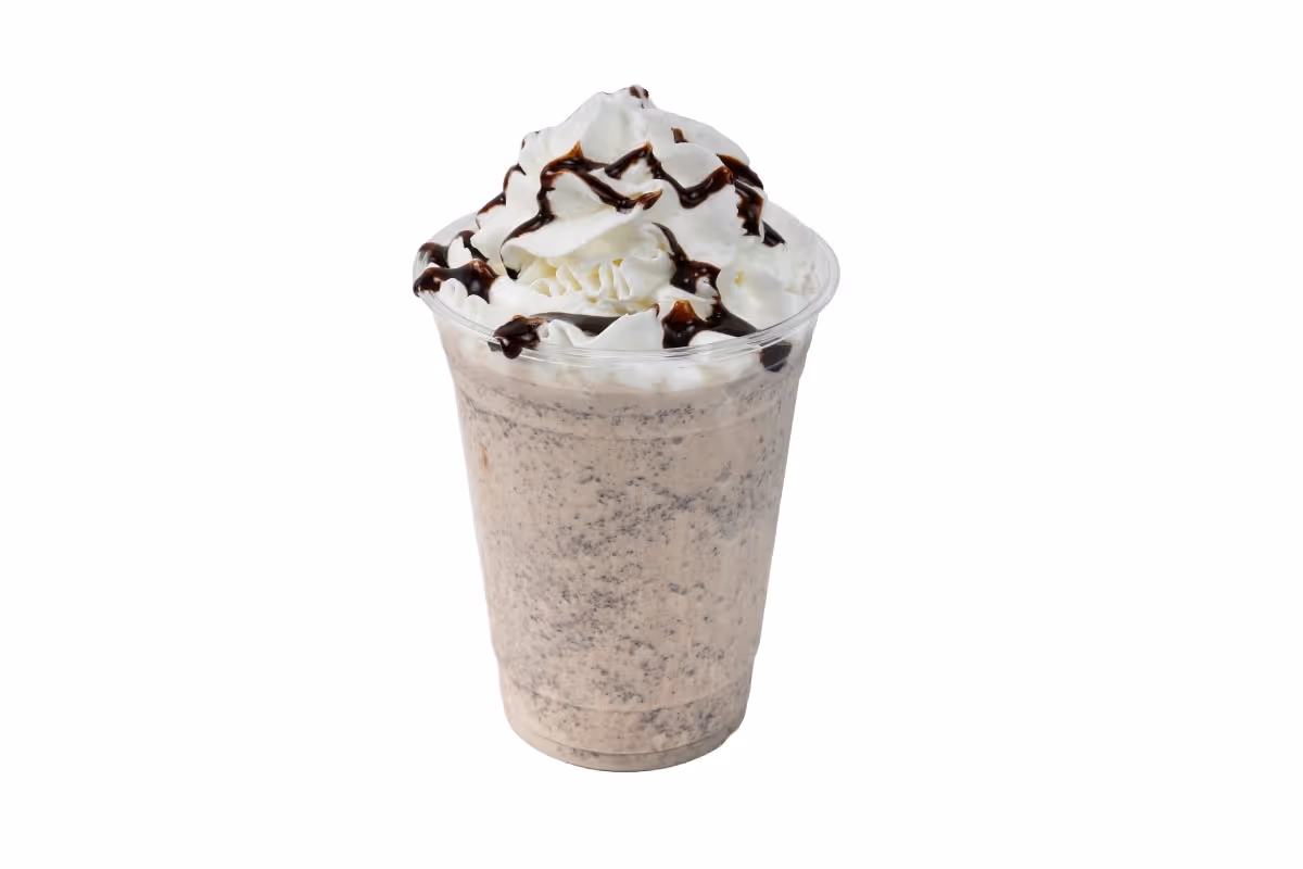 A cookies and cream milkshake in a clear cup, topped with whipped cream and chocolate syrup, on a white background.