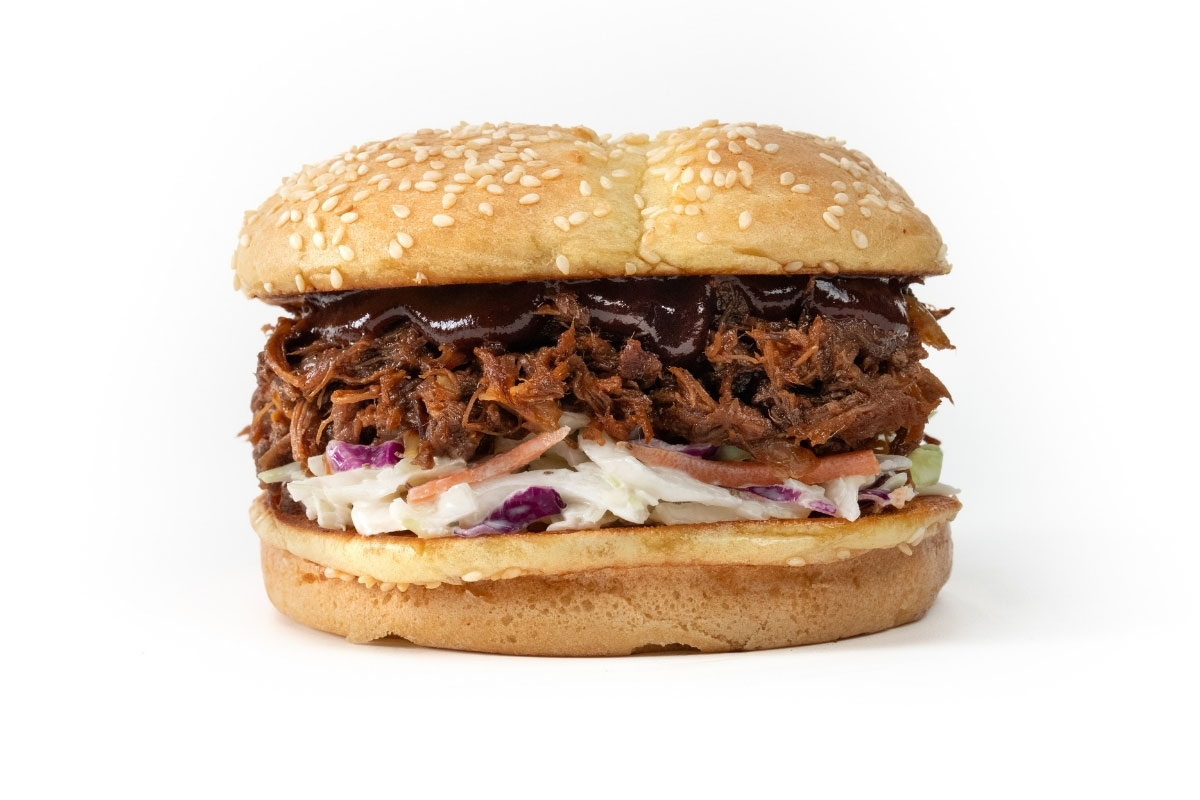 Pulled pork sandwich with barbecue sauce and coleslaw on a sesame seed bun, photographed on a white background.