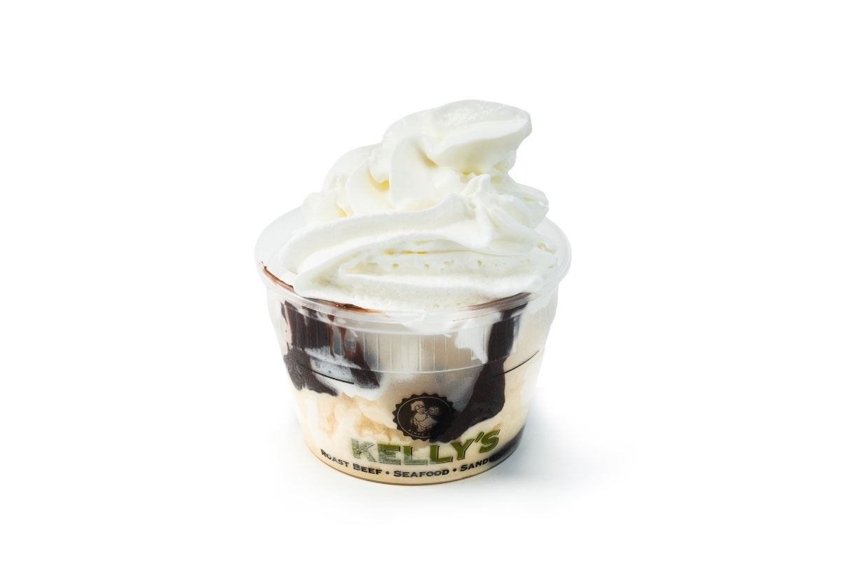 A cup of vanilla soft-serve ice cream with chocolate syrup in a branded Kelly’s plastic container on a white background.