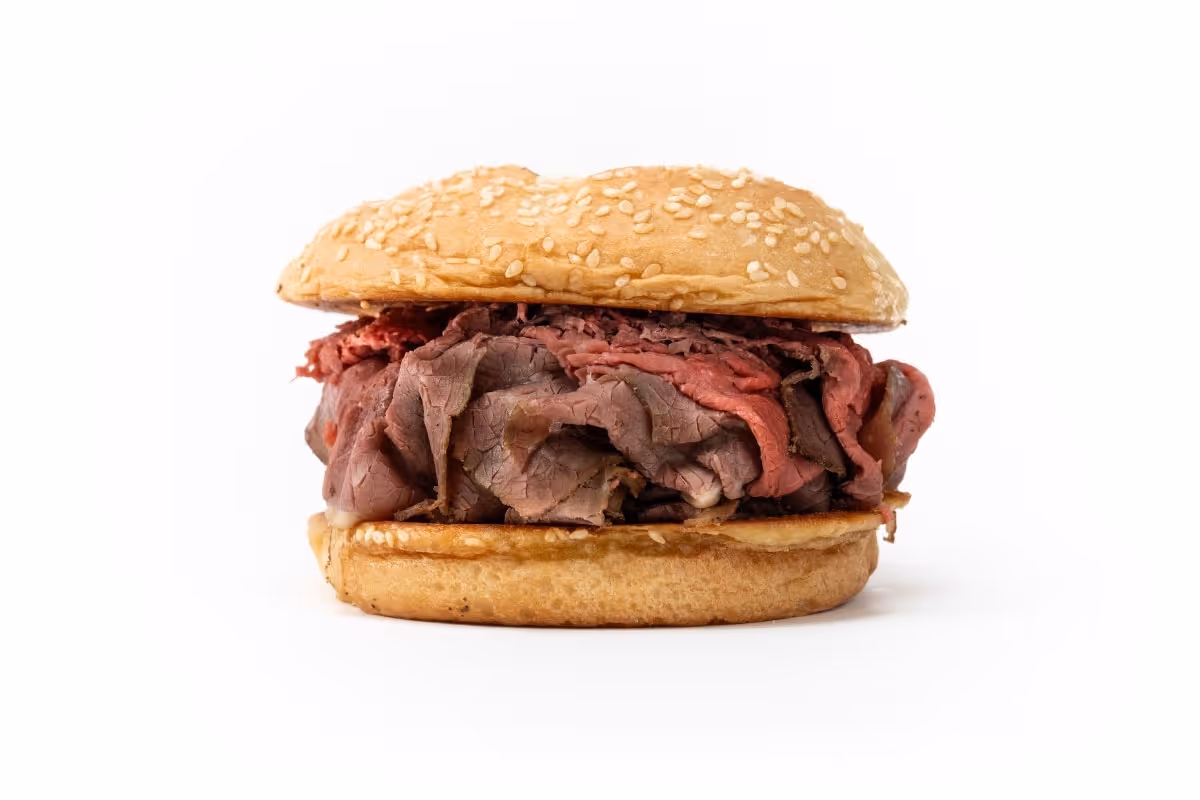 A roast beef sandwich on a sesame seed bun, filled with sliced roast beef, against a white background.