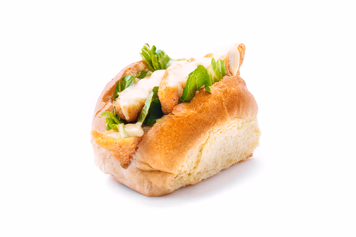 A sandwich roll filled with fried chicken pieces, lettuce, and mayonnaise on a white background.