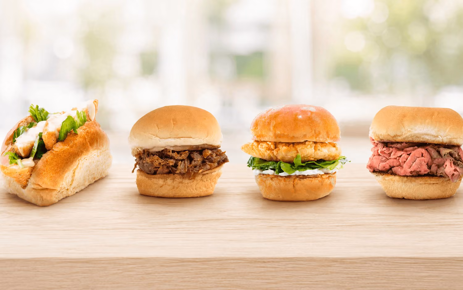 Four different sandwiches, each with various fillings, arranged in a row on a wooden surface against a blurred background.