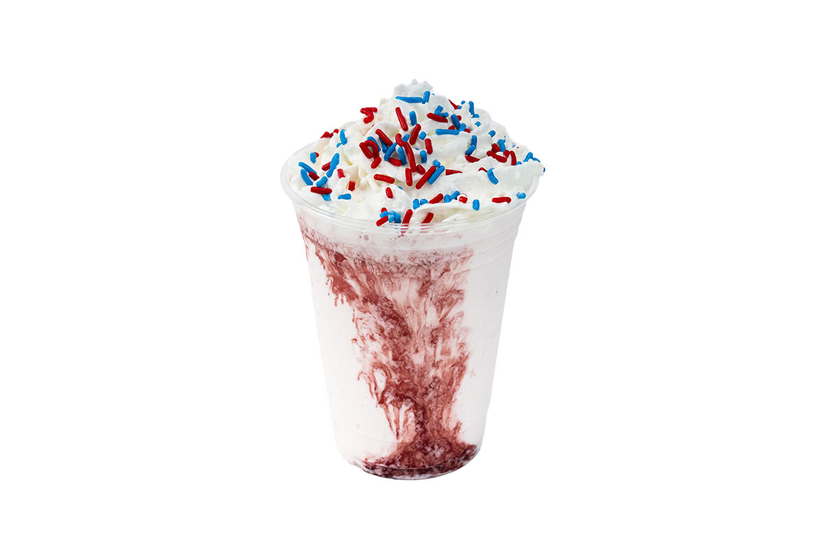 A vanilla milkshake in a clear cup with red swirls, topped with whipped cream and red, blue, and white sprinkles.