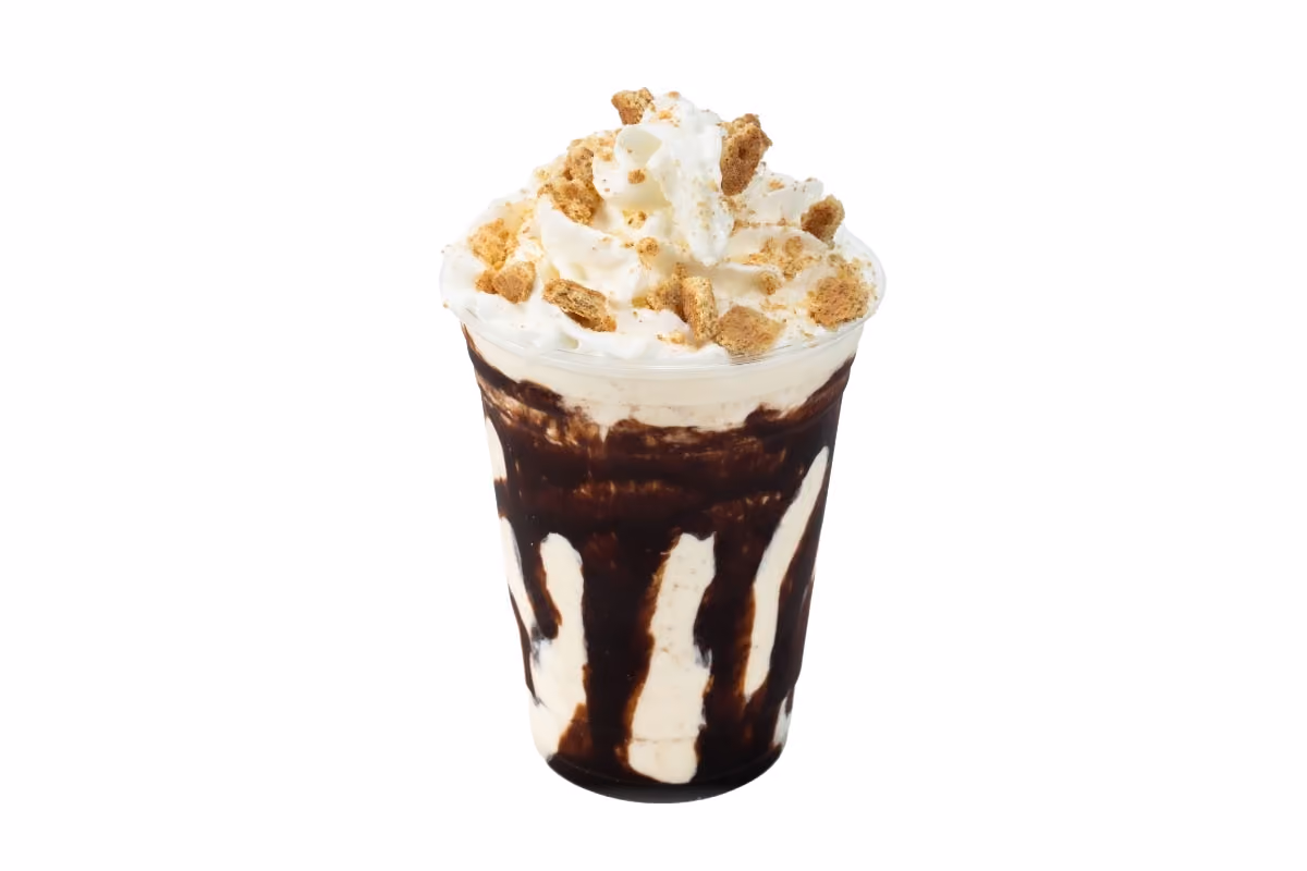A chocolate milkshake topped with whipped cream and crushed cookie crumbs in a clear plastic cup, isolated on white background.