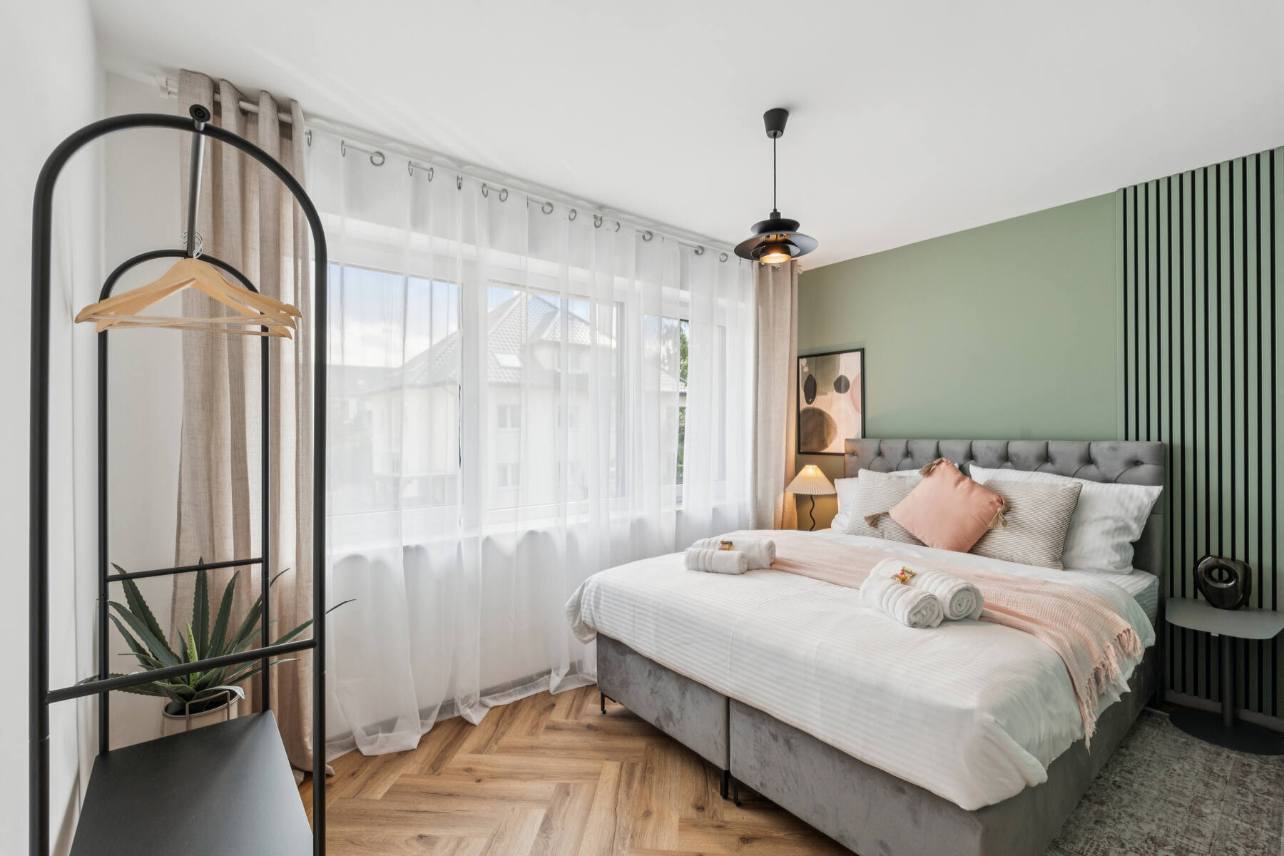 Schlafzimmer mit Doppelbett, rosa Tagesdecke, weißen Handtüchern und stilvollen Wandbildern – gemütlich und modern eingerichtet