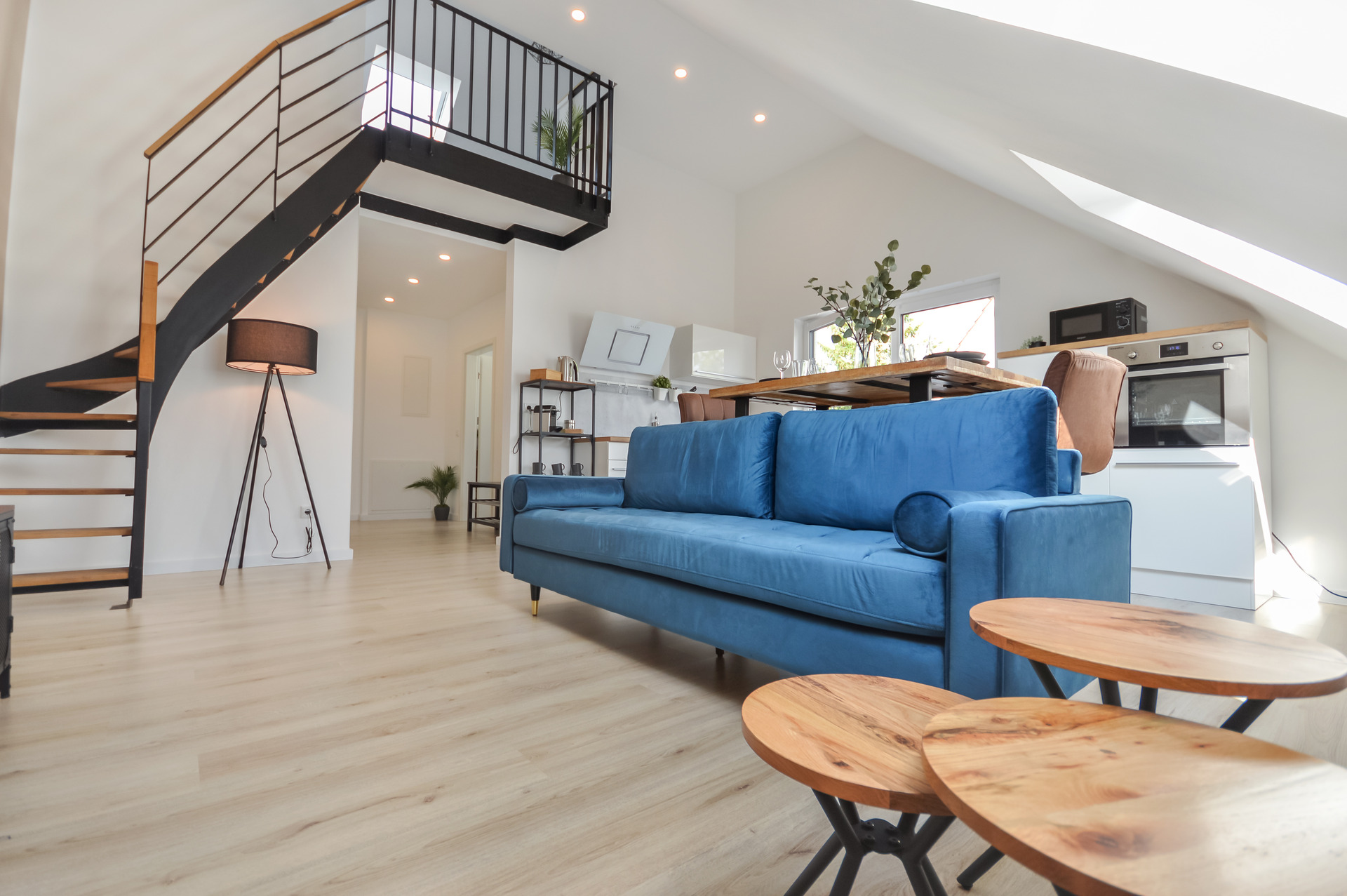 Moderne Loftwohnung mit einer blauen Couch im Manchester-Stil, im Hintergrund eine Küche und eine Stahltreppe zum Studio