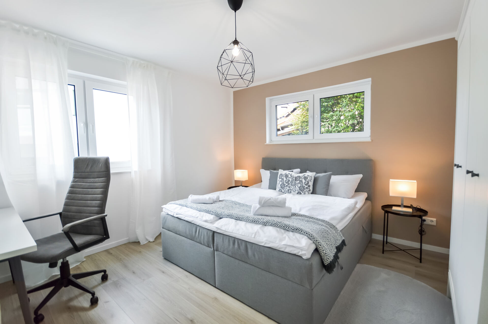 Helles Schlafzimmer in Bielefeld-Brackwede mit großem Doppelbett in Grau, stilvollen Nachttischen, modernem Schreibtisch mit Bürostuhl und warmen Naturtönen – ideal für erholsame Nächte und produktives Arbeiten.