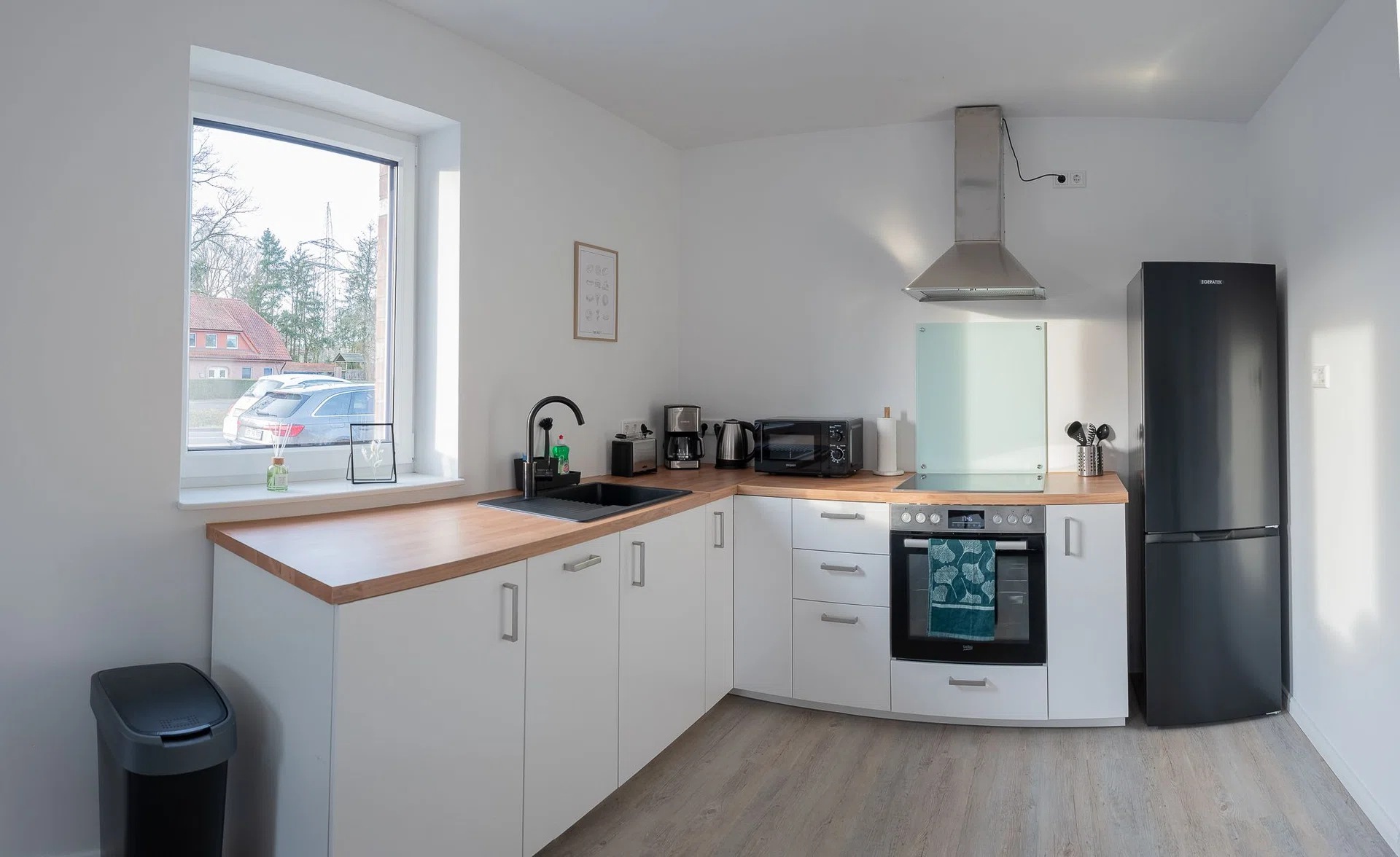 Weiße Winkelküche mit Holzarbeitsplatte, Backofen und Kühlschrank