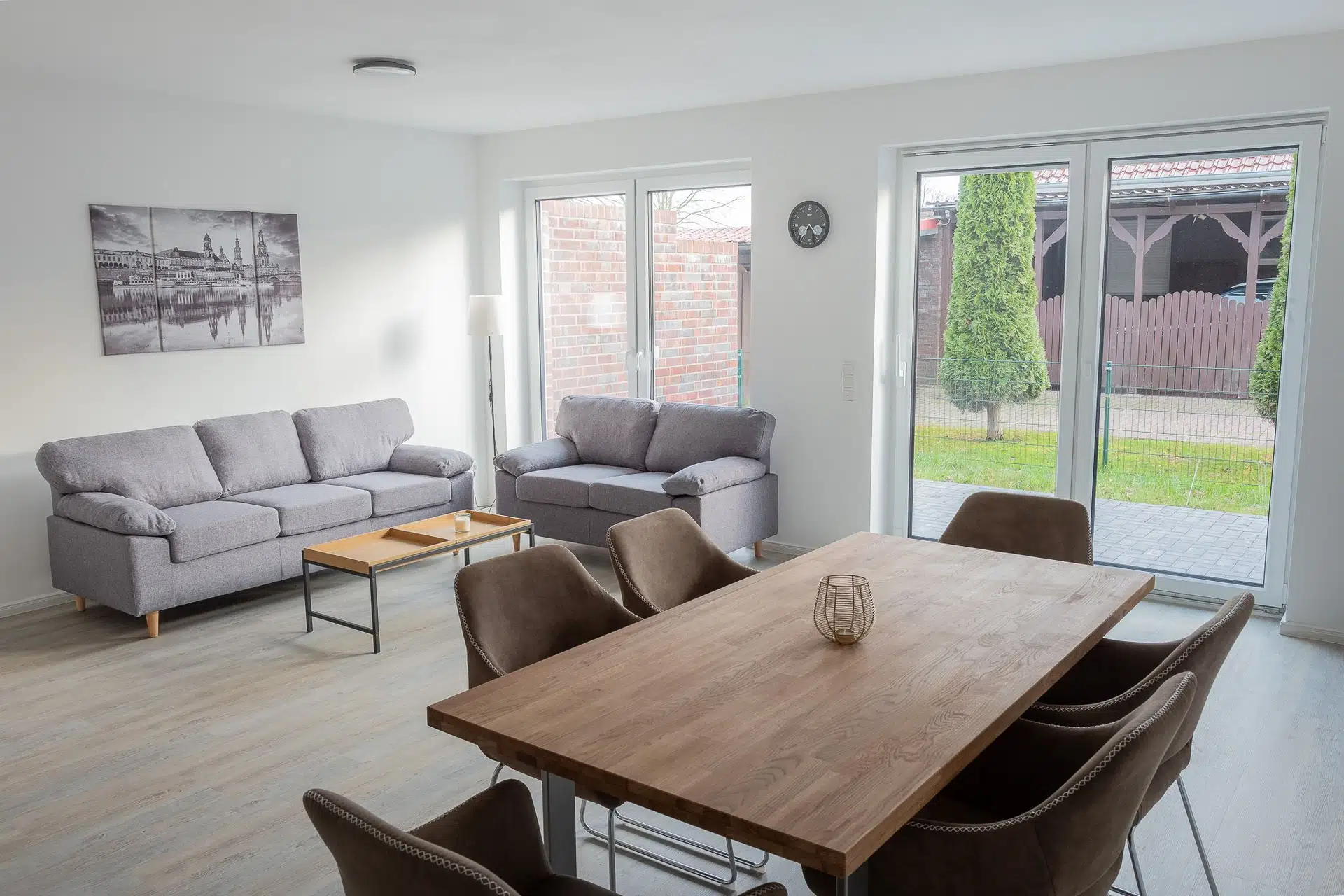 Offener Wohn- und Essbereich mit grauem Sofa, Holztisch und Gartenblick